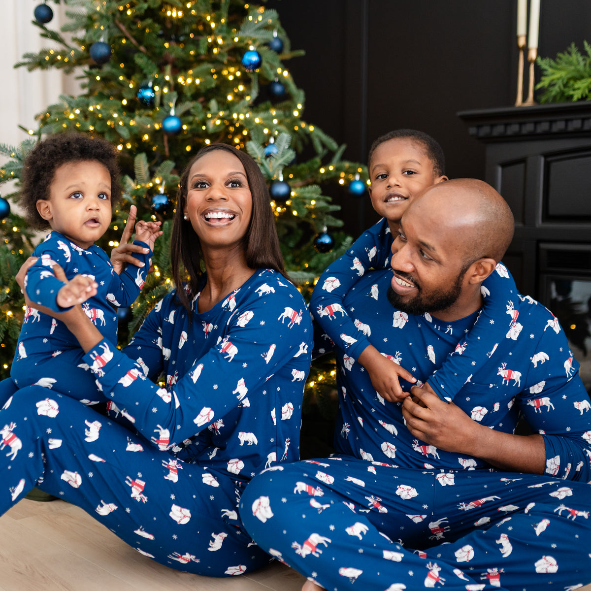 Family of four sitting on the floor all matching the holiday print Frosty Friends pajamas