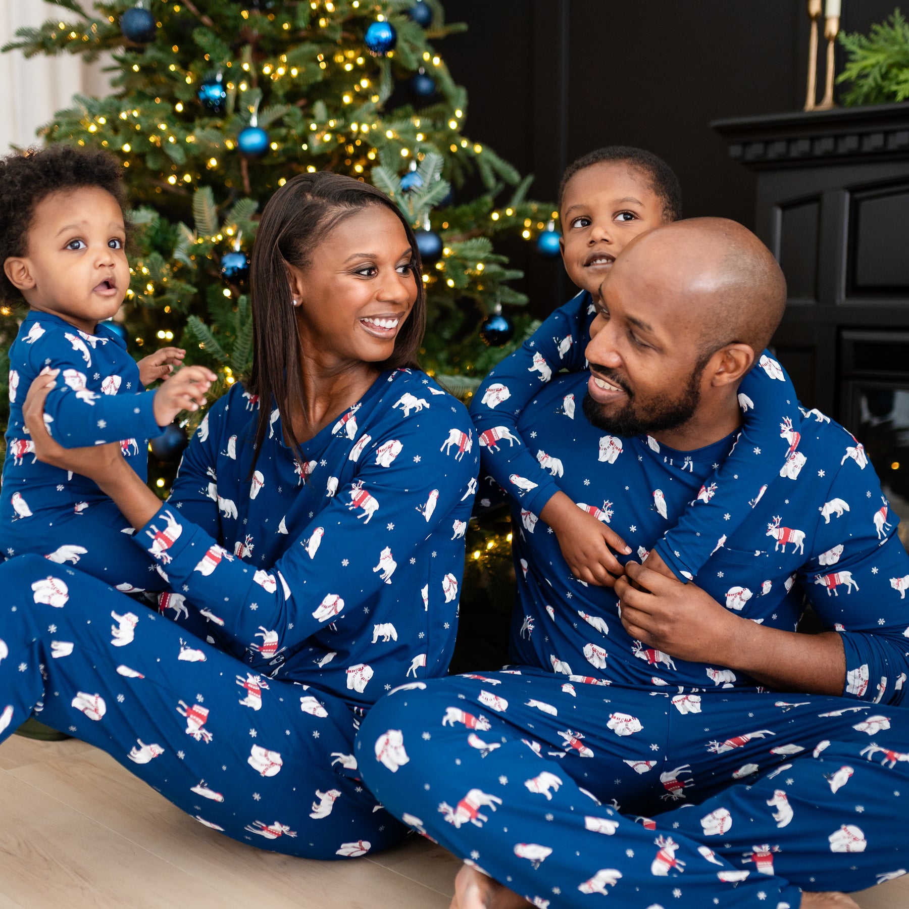 Family of four sitting on the floor matching in various items in the holiday print Frosty Friends