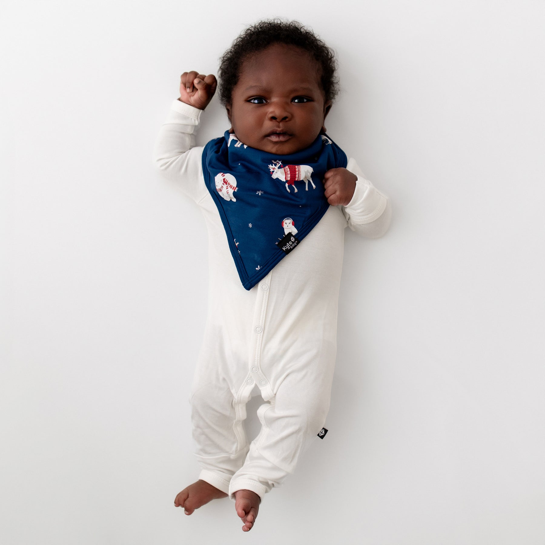 Newborn baby laying on a white blanket wearing the Bib in Frosty Friends and Cloud Snap Romper 