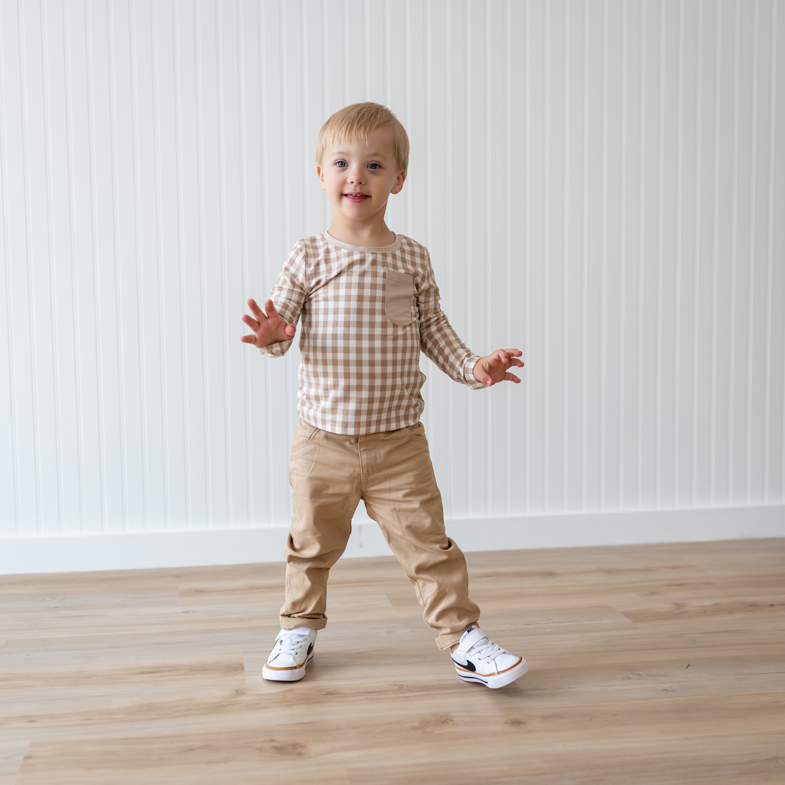 Young boy walking wearing the Long Sleeve Toddler Crew Neck Tee in Gingham Bisque and khaki colored pants
