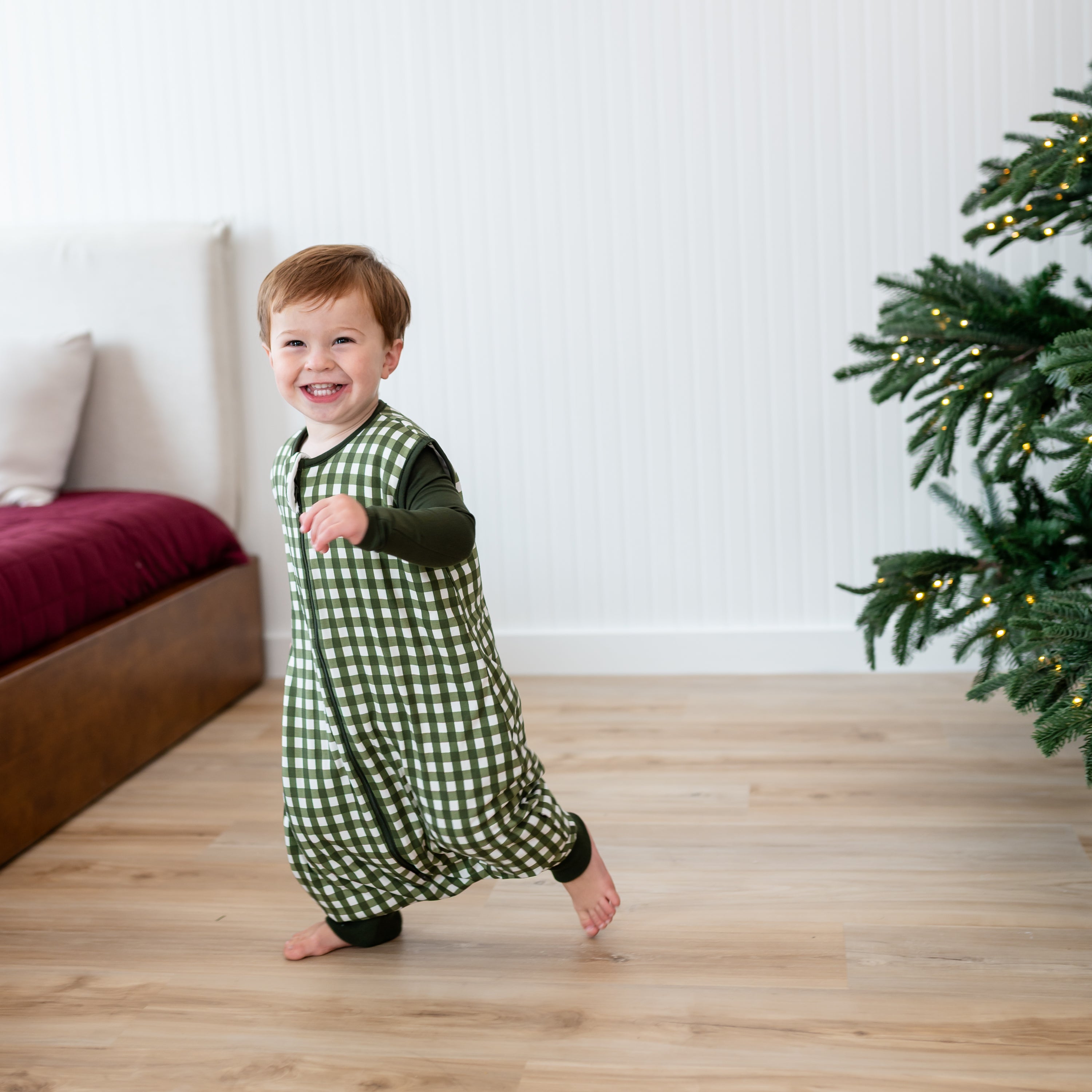 Smiling toddler walking around wearing the Sleep Bag Walker in Gingham Fir 1.0