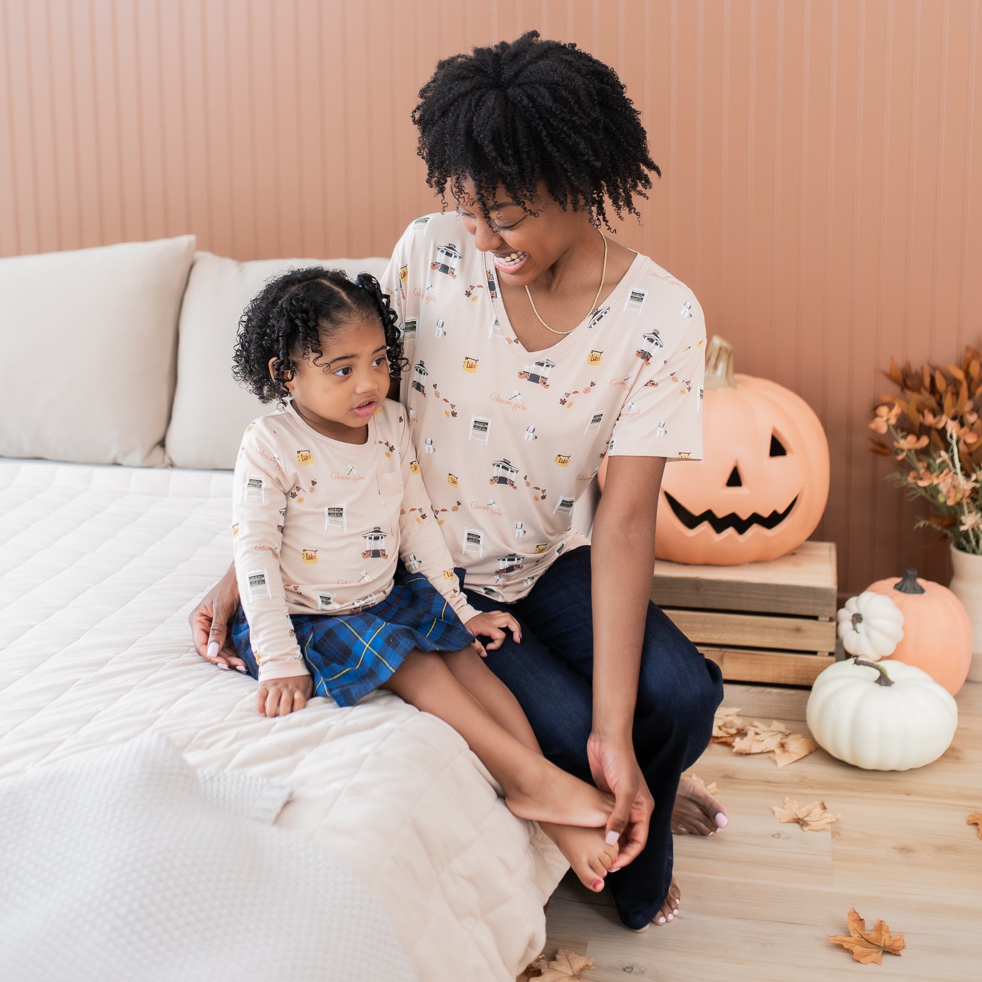 Mother and daughter sitting on a bed both matching in Gilmore Girls themed shirts
