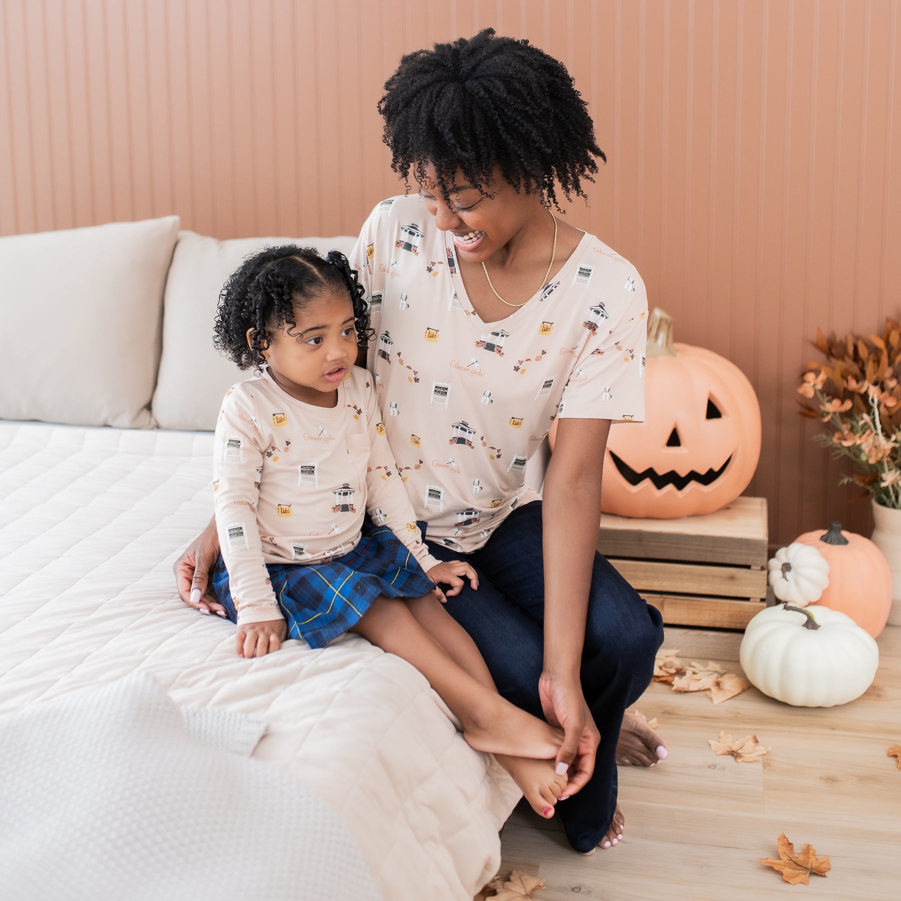 Mother and daughter sitting on a bed both matching in Gilmore Girls themed shirts