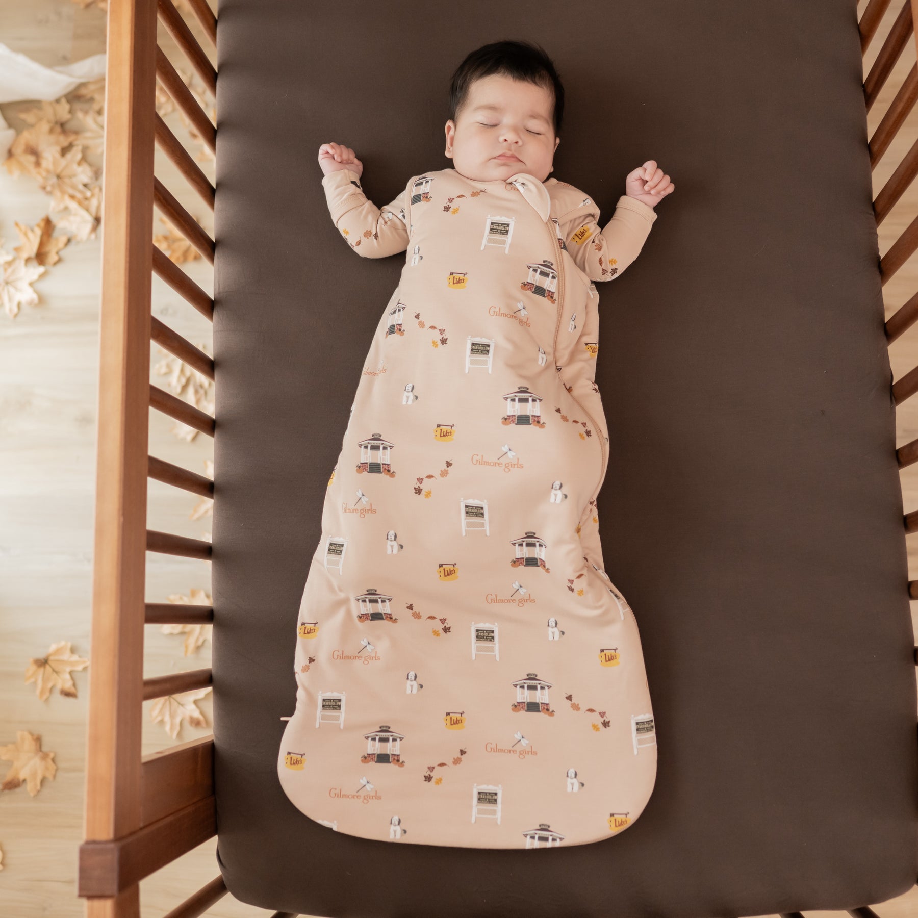Sleeping infant laying in a crib on an Espresso crib sheet wearing the Sleep Bag in Gilmore Girls 1.0 and matching romper