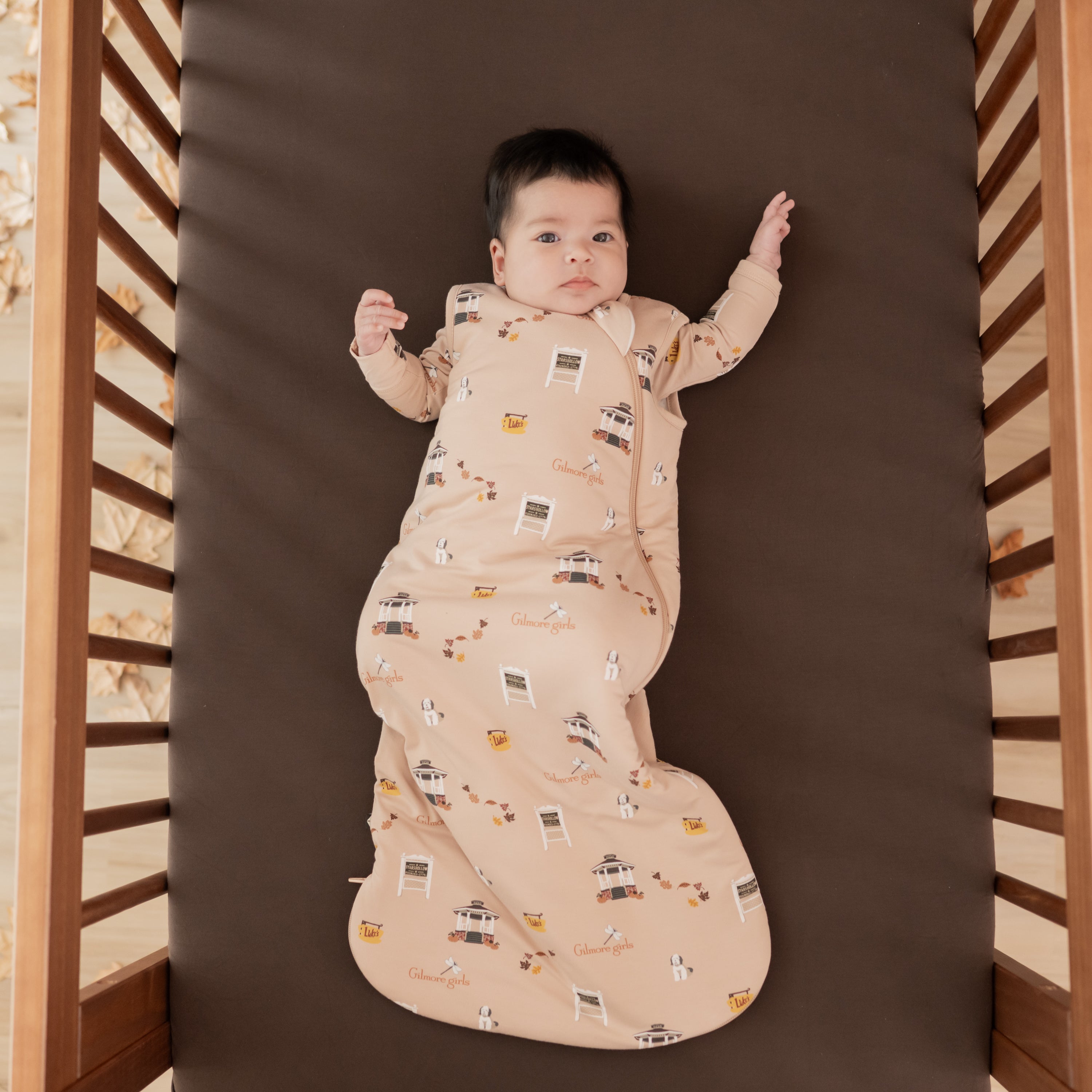 Infant laying in a crib on an Espresso Crib sheet wearing the Sleep Bag in Gilmore Girls 1.0 with a matching romper on underneath
