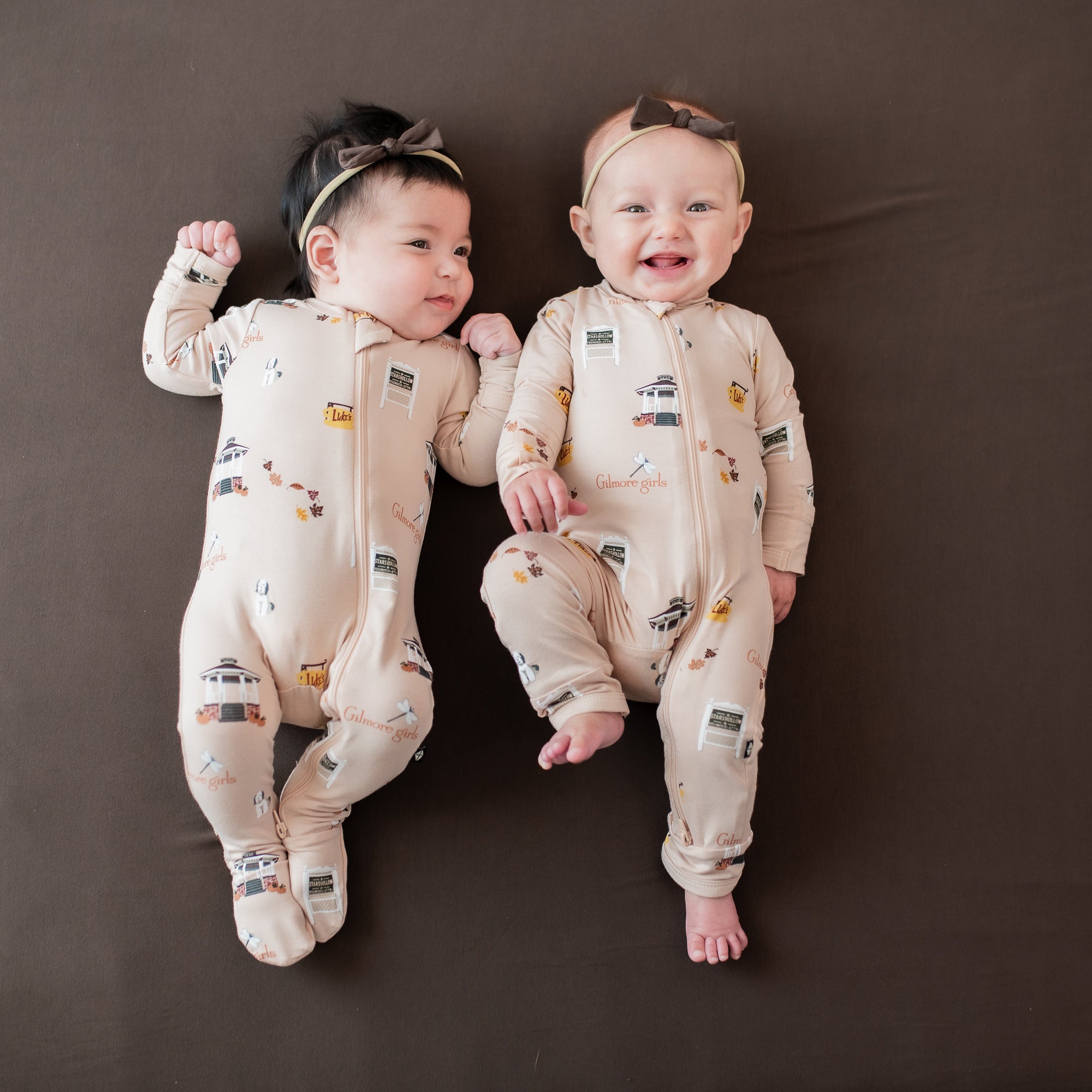 Two infants laying side by side wearing the Zippered Footie and Zippered romper in Gilmore Girls with Tiny Nylon Bows in Espresso