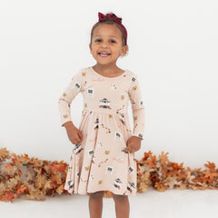 Young girl wearing the Long Sleeve Twirl Dress in Gilmore Girls with a burgundy bow in front of a white backdrop and a leaf garland