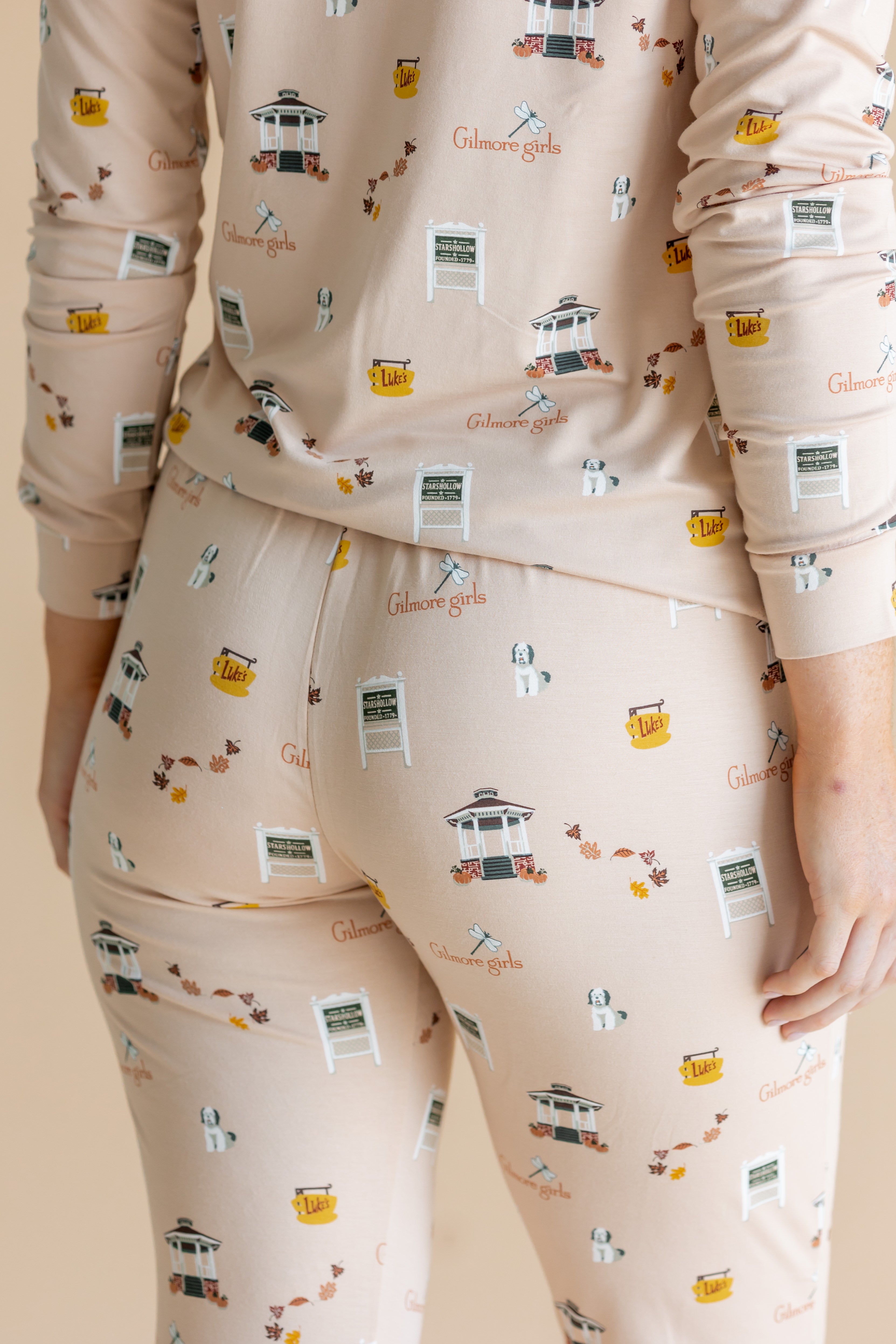A close-up of a person wearing a matching long-sleeve pajama top and leggings set in a light beige color, printed with a  Gilmore Girls inspired print.