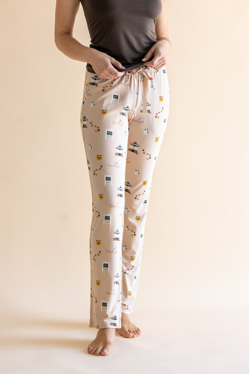 A person wearing cream-colored lounge pants with a Gilmore Girls inspired pattern, paired with a dark gray top, standing against a solid beige background.