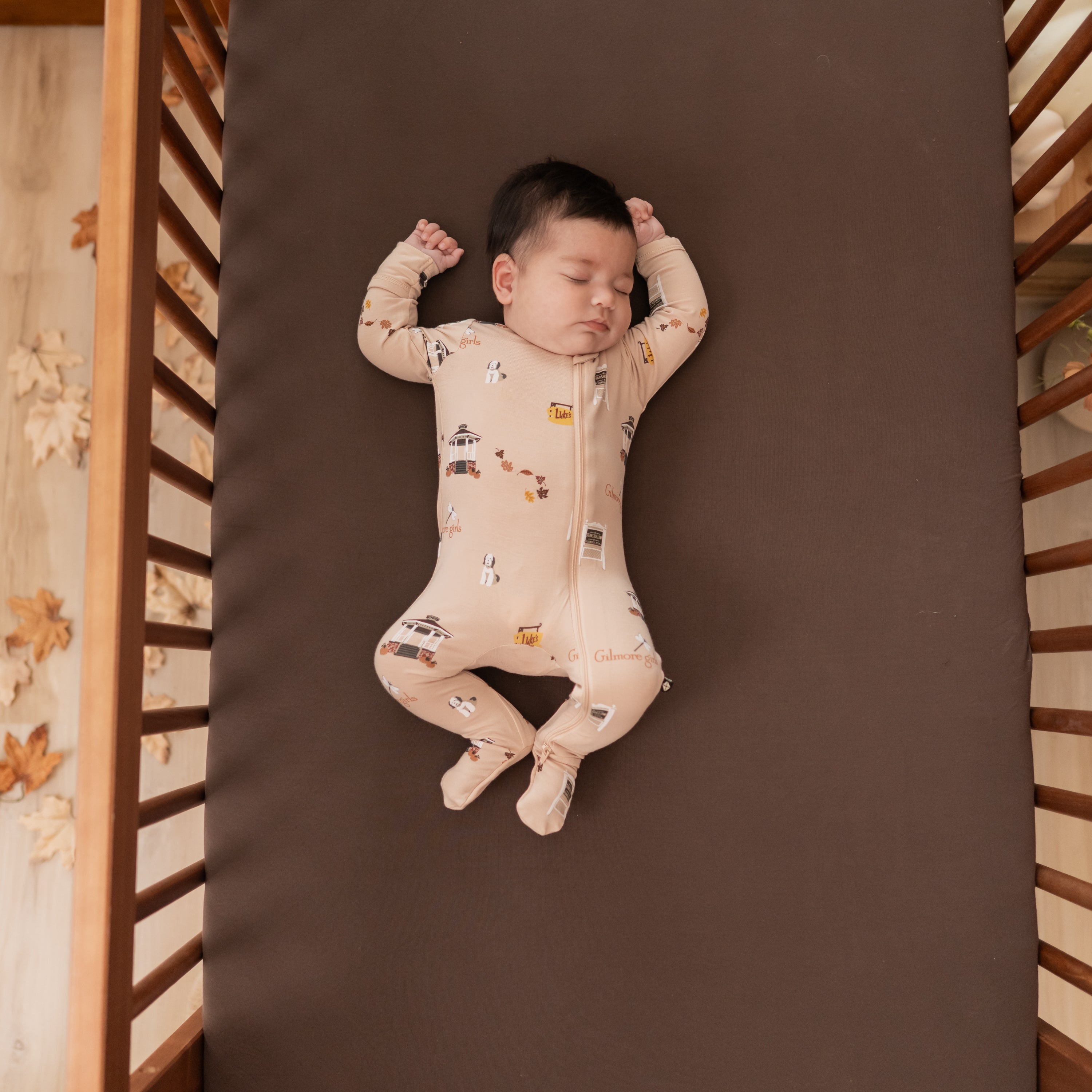 Sleeping infant laying in a crip on an Espresso crib sheet wearing the Zippered Footie in Gilmore Girls