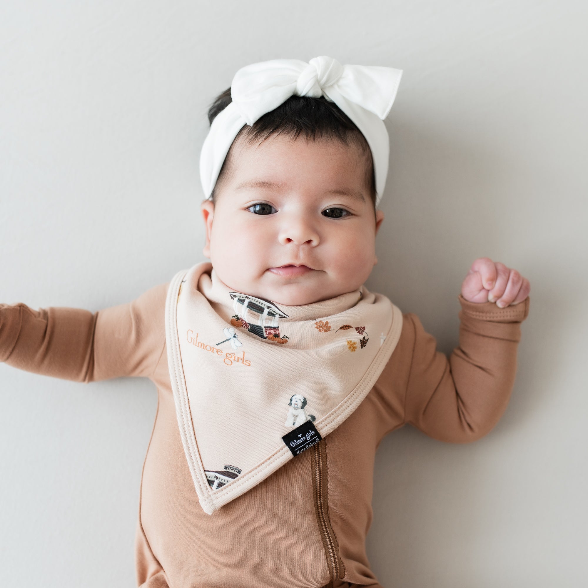 Infant wearing the Bib in Gilmore Girls paired with a Latte zippered romper and a White bow