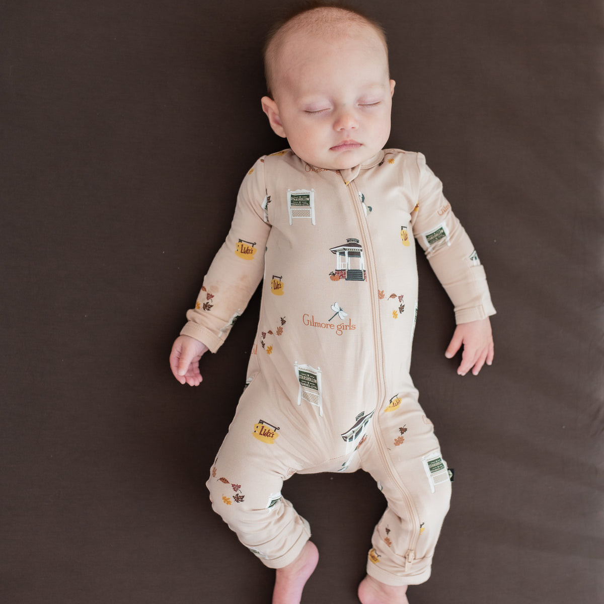Sleeping infant wearing the Zippered Romper in Gilmore Girls laying on an Espresso crib sheet