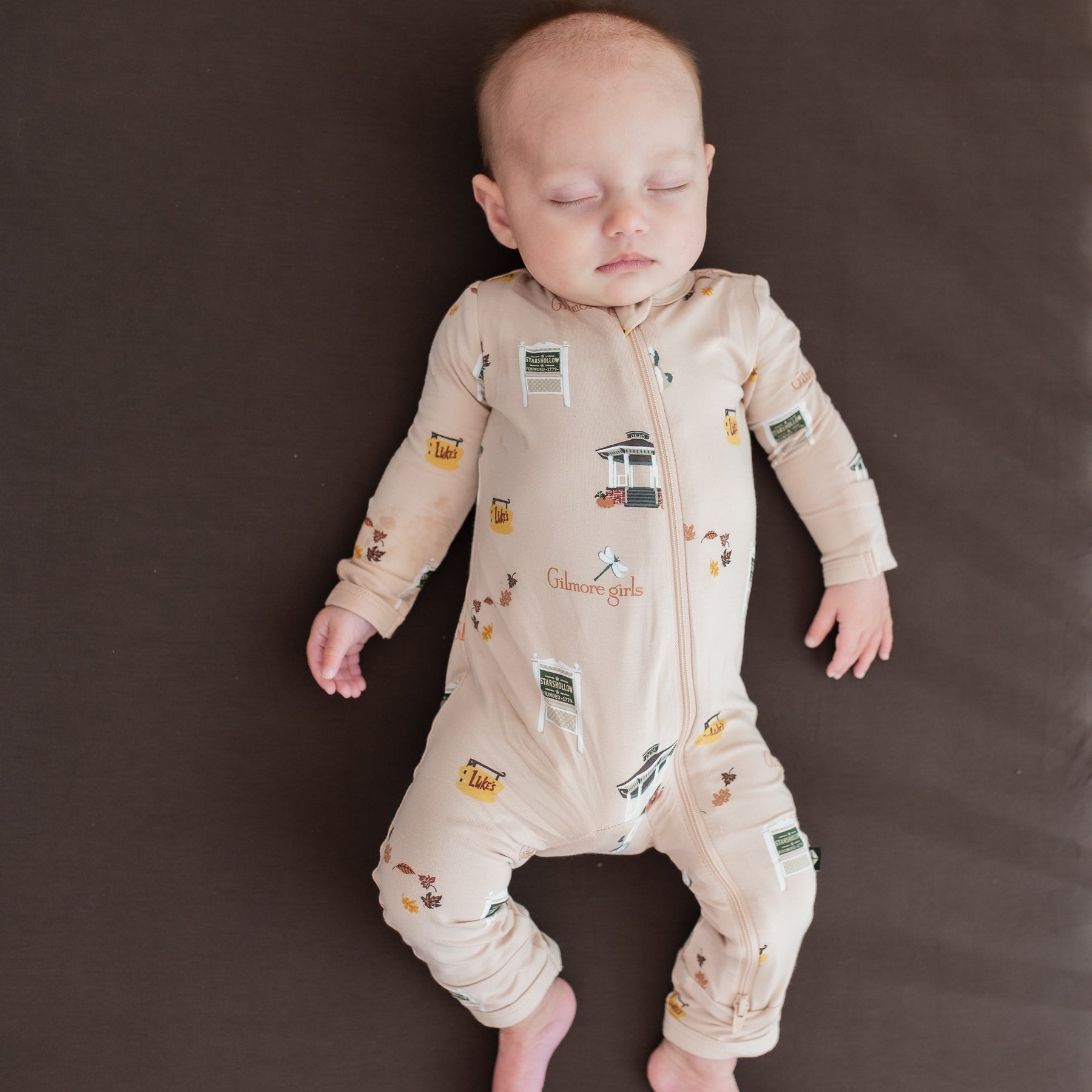 Sleeping infant wearing the Zippered Romper in Gilmore Girls laying on an Espresso crib sheet