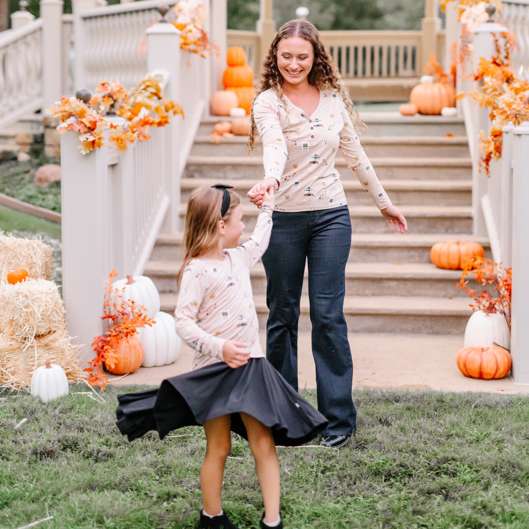 Mother holding daughters hand while daughter is twirling wearing a Gilmore Girls themed shirt and black twirl dress on underneath outside in front of a fall decorated gazebo