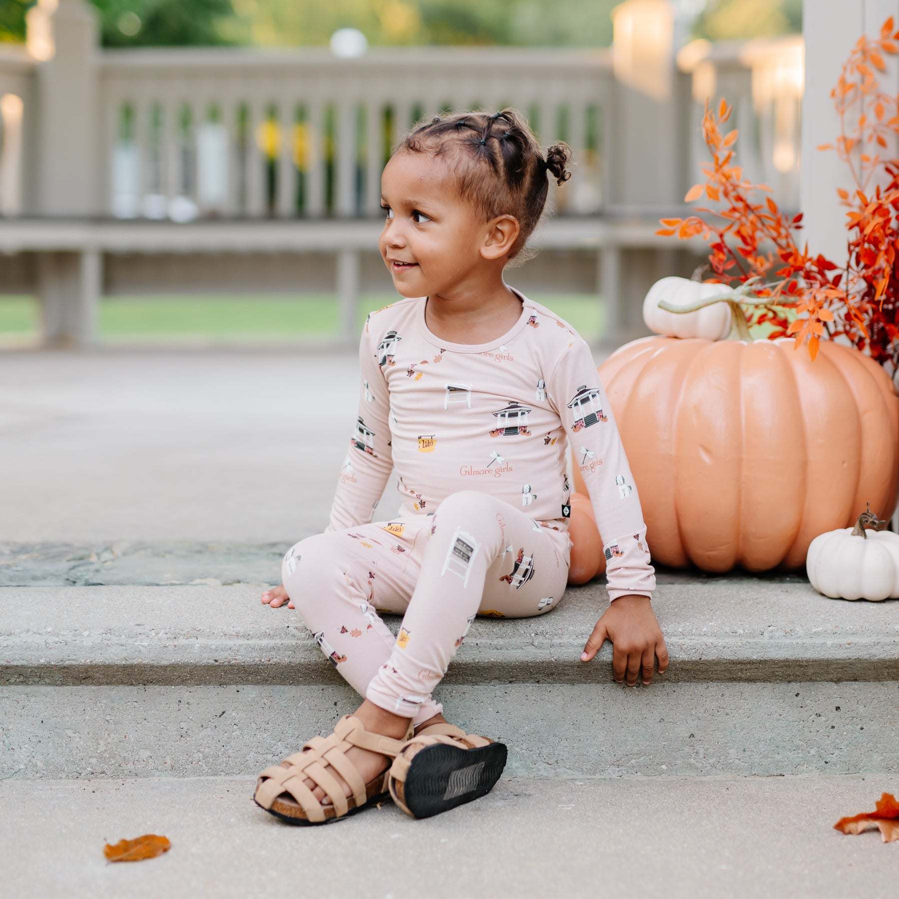 Young girl sitting on stone steps in front of decorative pumpkins wearing the Long Sleeve Pajamas in Gilmore Girls