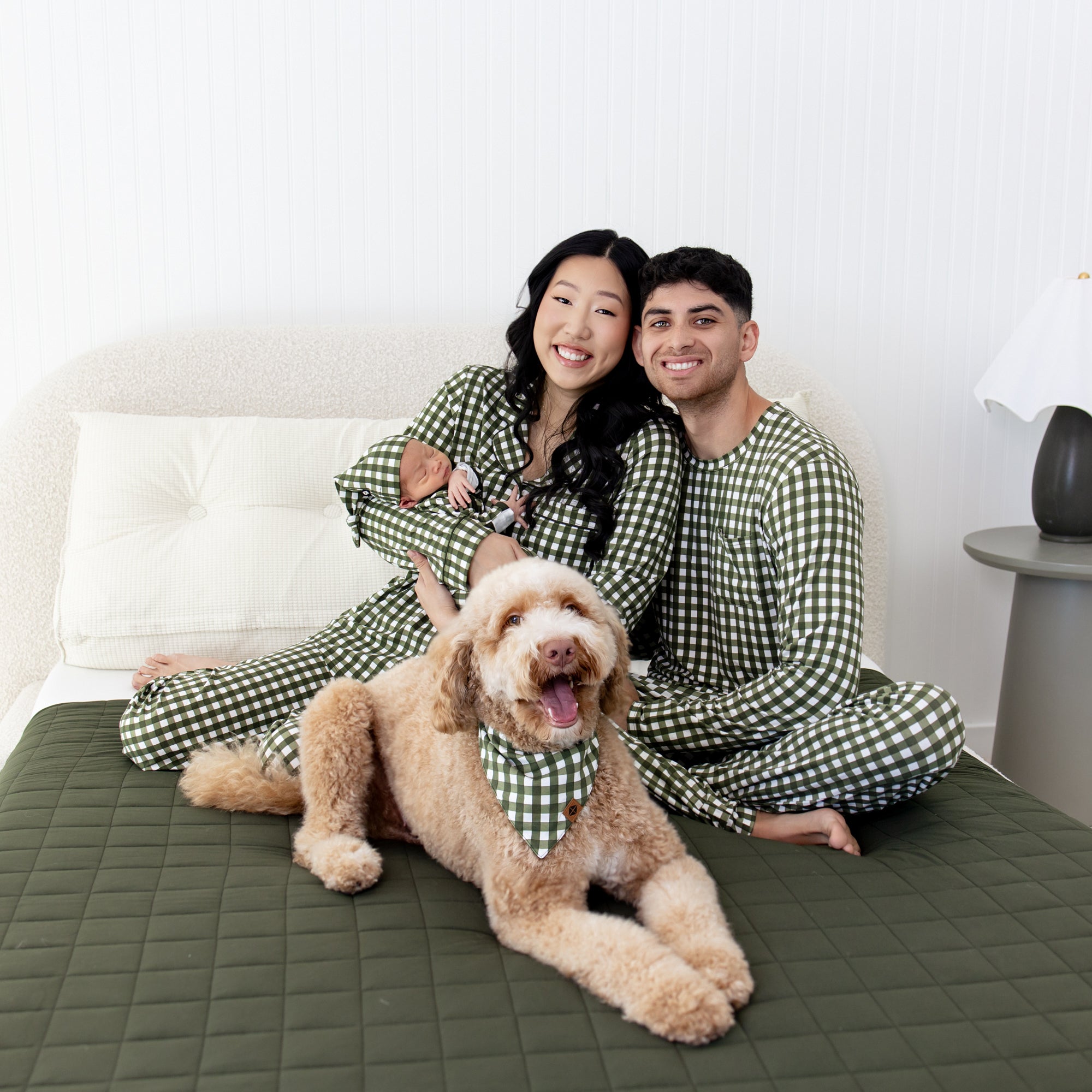 Family in matching green gingham patterns pajamas with a dog on a cozy bed