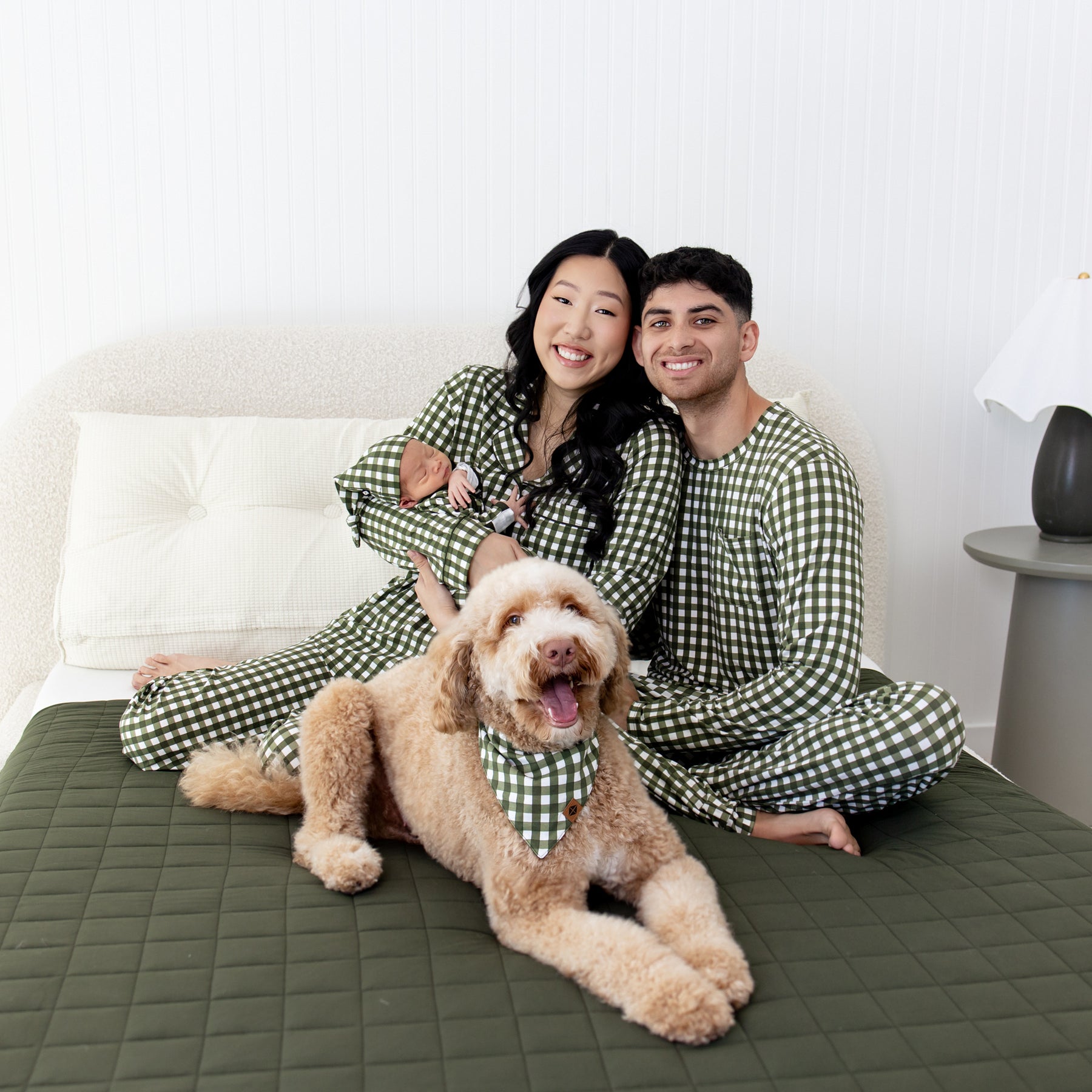 Family in matching green gingham patterns pajamas with a dog on a cozy bed