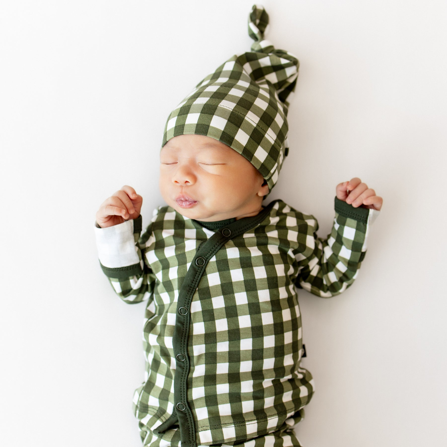 Newborn baby wearing a green and white checkered outfit and hat on a white background