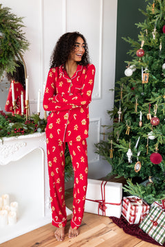 Woman wearing long sleeve women's pajama set in gingerbread print standing beside Christmas tree and presents