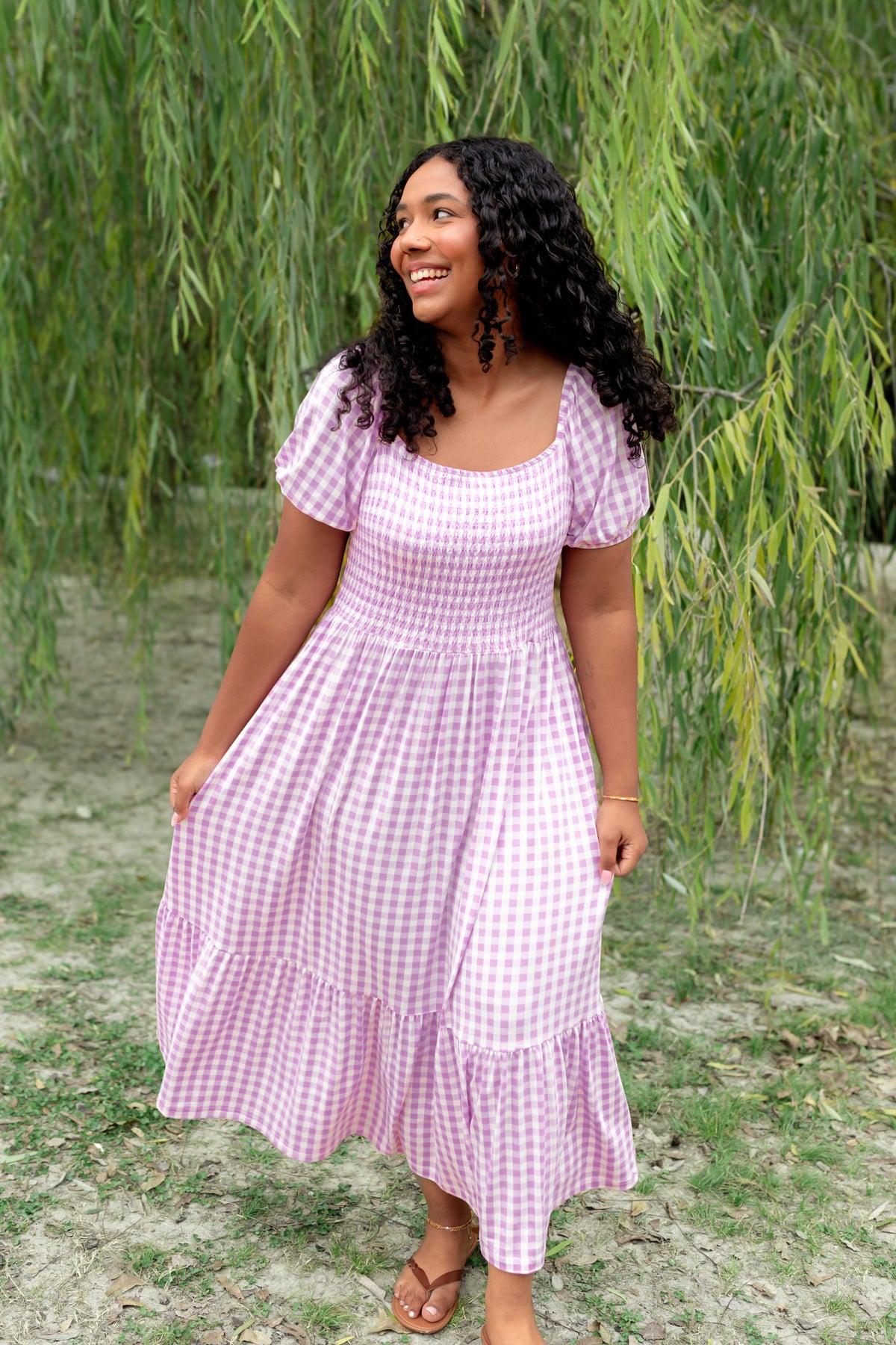 Female wearing the Women’s Smocked Dress in Gingham Thistle standing in a field in front of a tree
