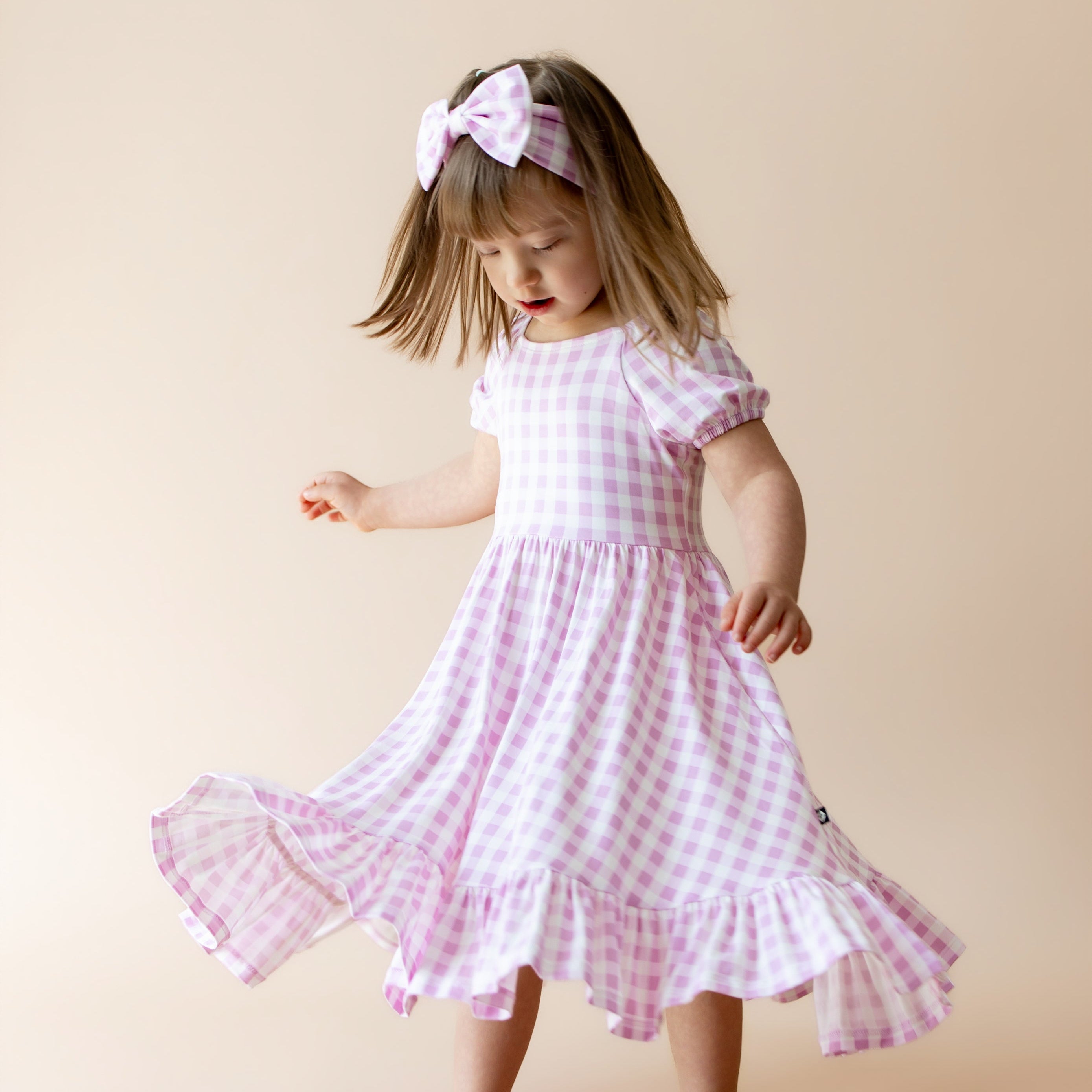Young girl twirling in a puff sleeve dress with purple gingham pattern and matching bow headband 