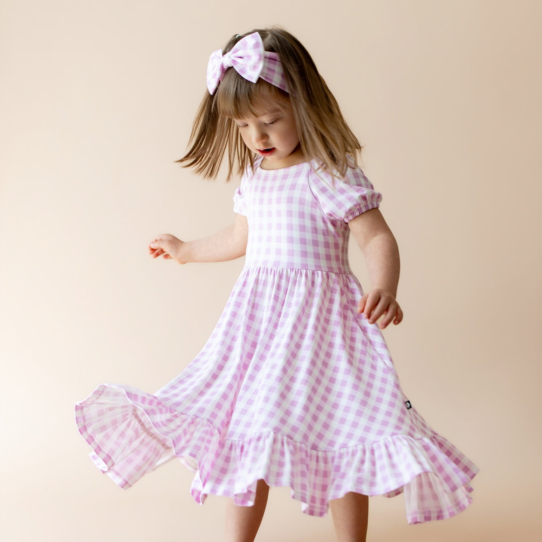 Young girl twirling in a puff sleeve dress with purple gingham pattern and matching bow headband 