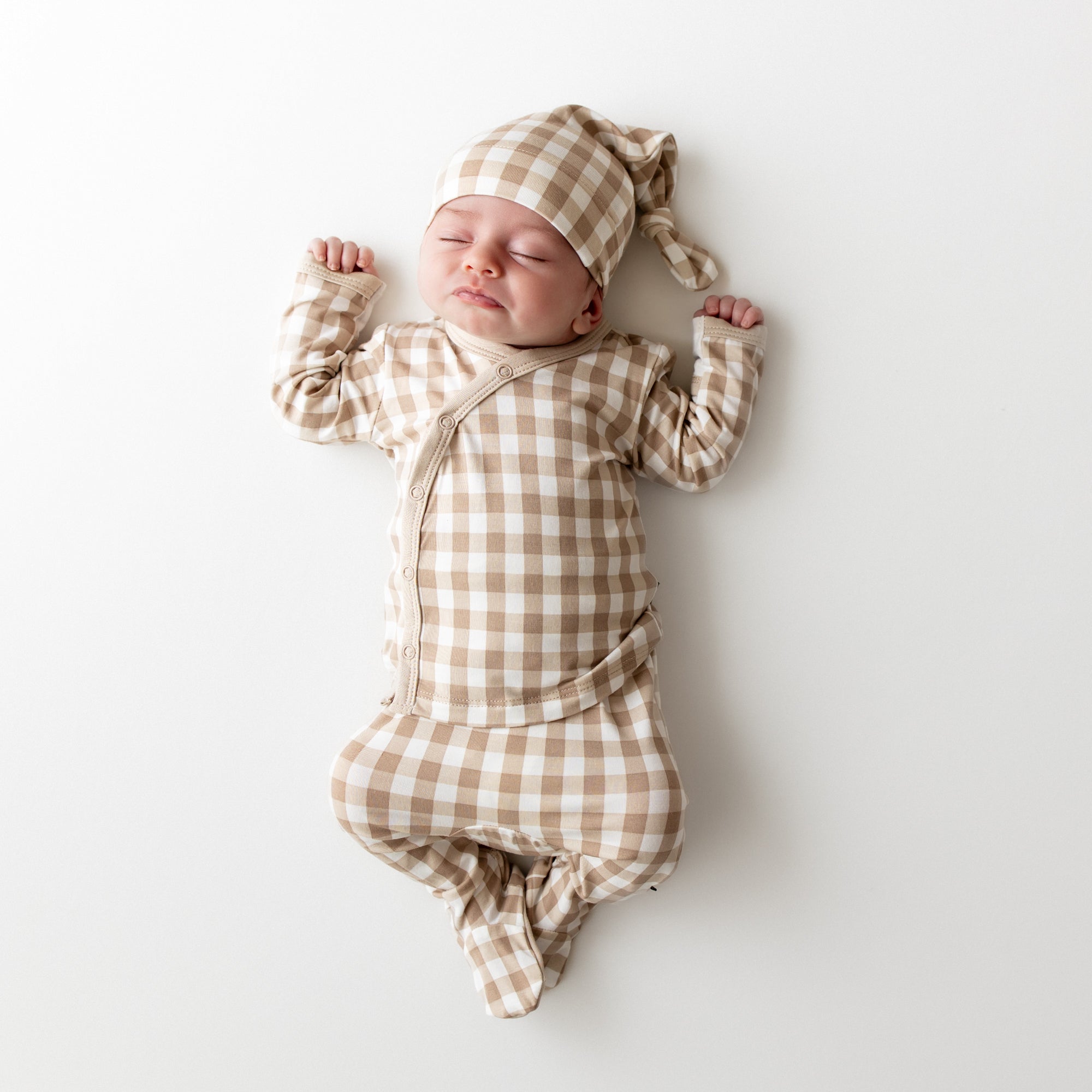Newborn laying down sleeping wearing the Take Me Home Set with Cap in Gingham Bisque
