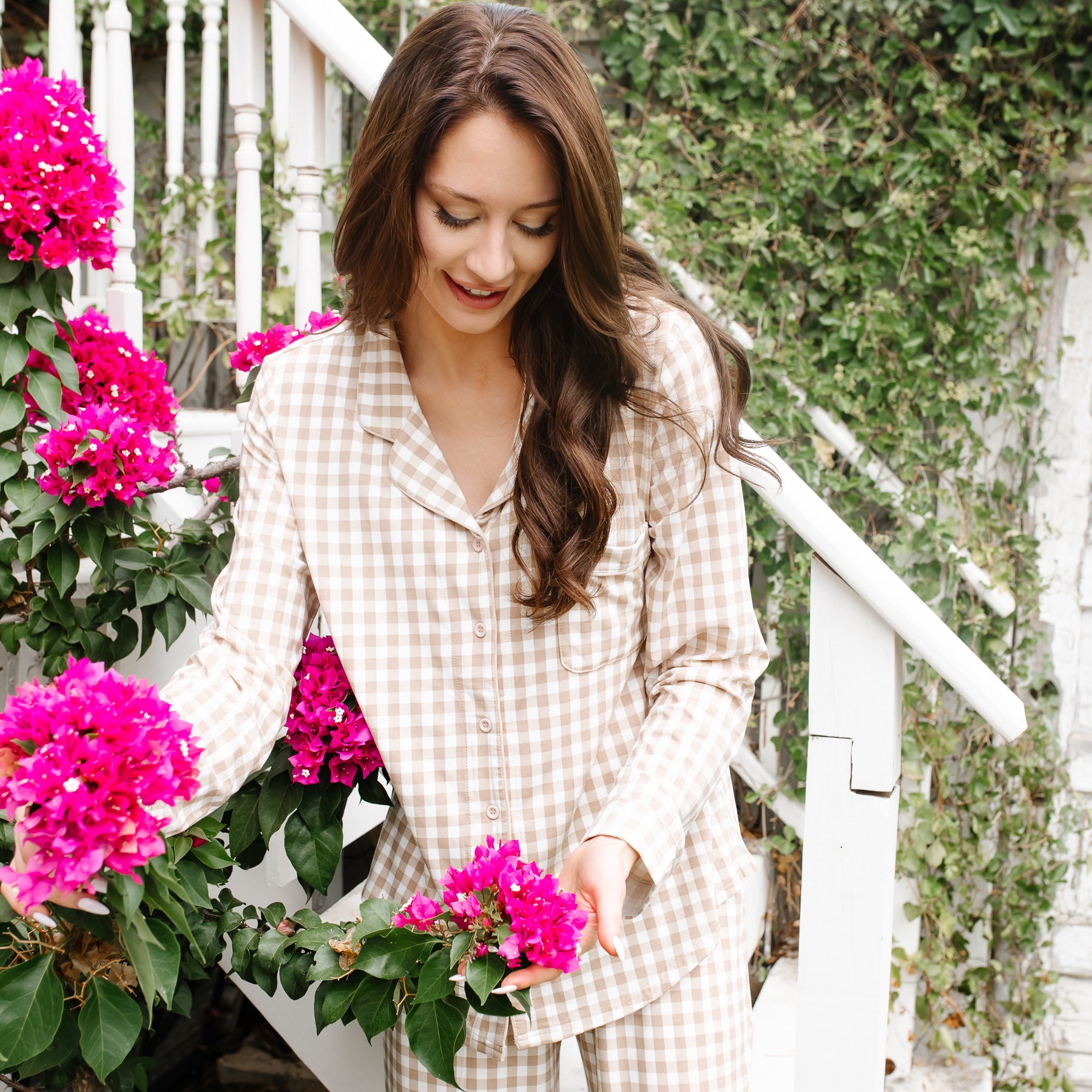 Close up of the Long-Sleeved Women's Pajama Set in Gingham Bisque shown on a female model standing on front steps holding pink colored flowers