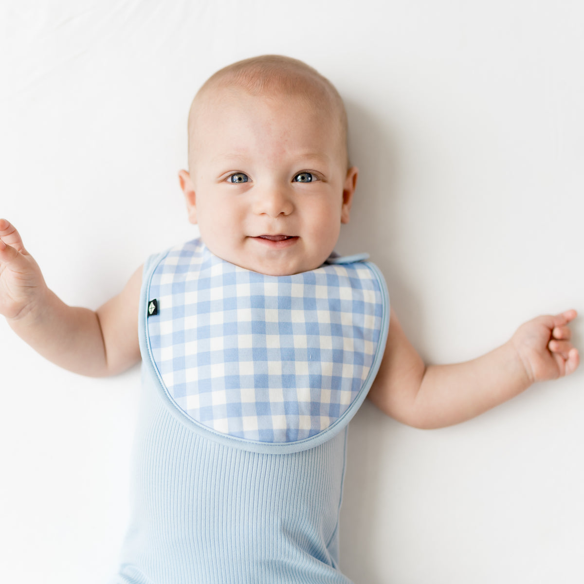Infant wearing the Cushy Bib in Gingham Breeze overtop a breeze sleeveless bodysuit