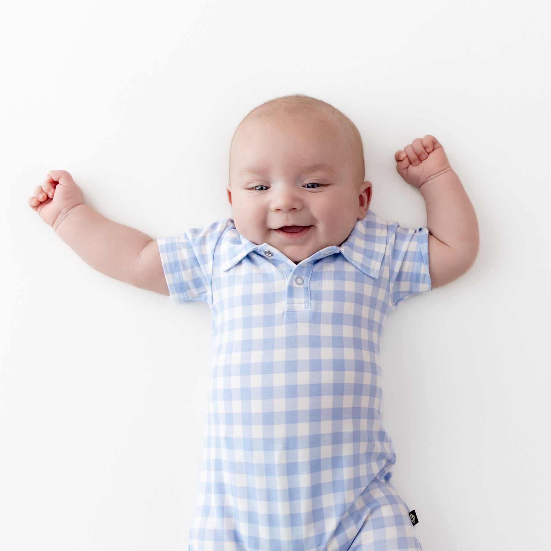 Close up of Polo Shortall in Gingham Breeze shown on an infant laying on a light cream surface