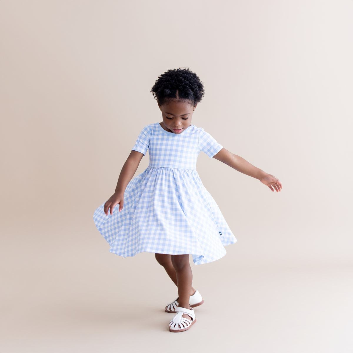 Young girl twirling wearing the Twirl Dress in Gingham Breeze
