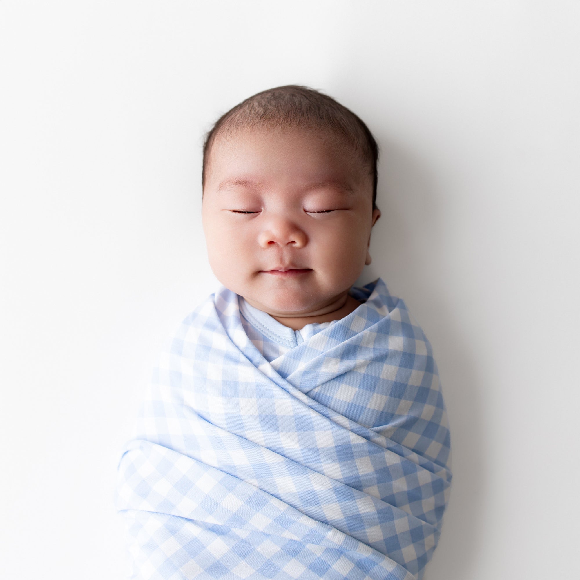 Close up of sleeping infant swaddled in the Swaddle Blanket in Gingham Breeze