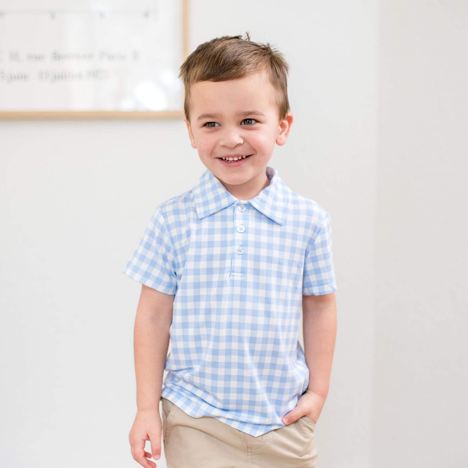 Smiling boy wearing the Toddler Short Sleeve Polo in Gingham Breeze with khaki colored pants