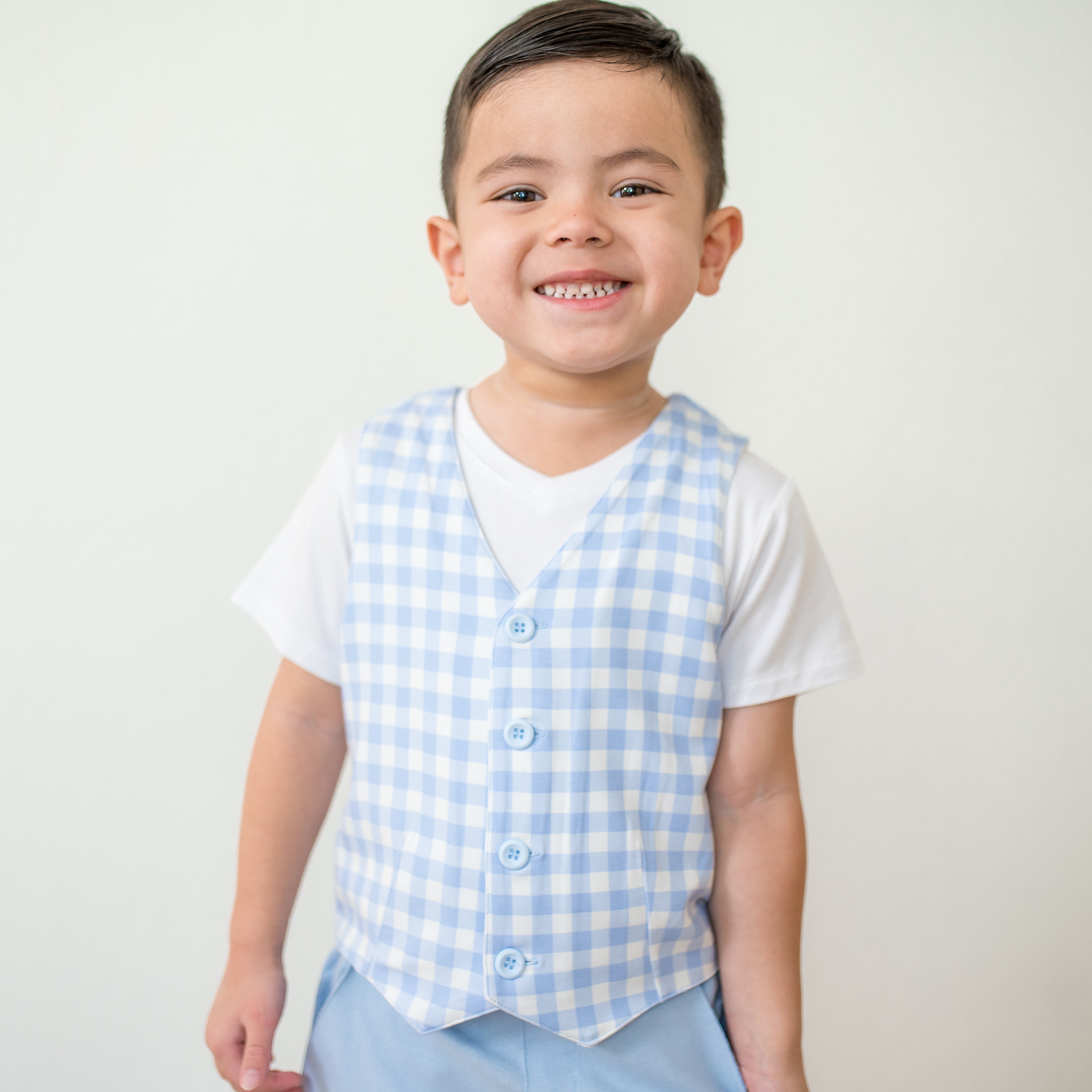 Young smiling boy wearing the Tuxedo Vest in Gingham Breeze overtop a white v-neck shirt