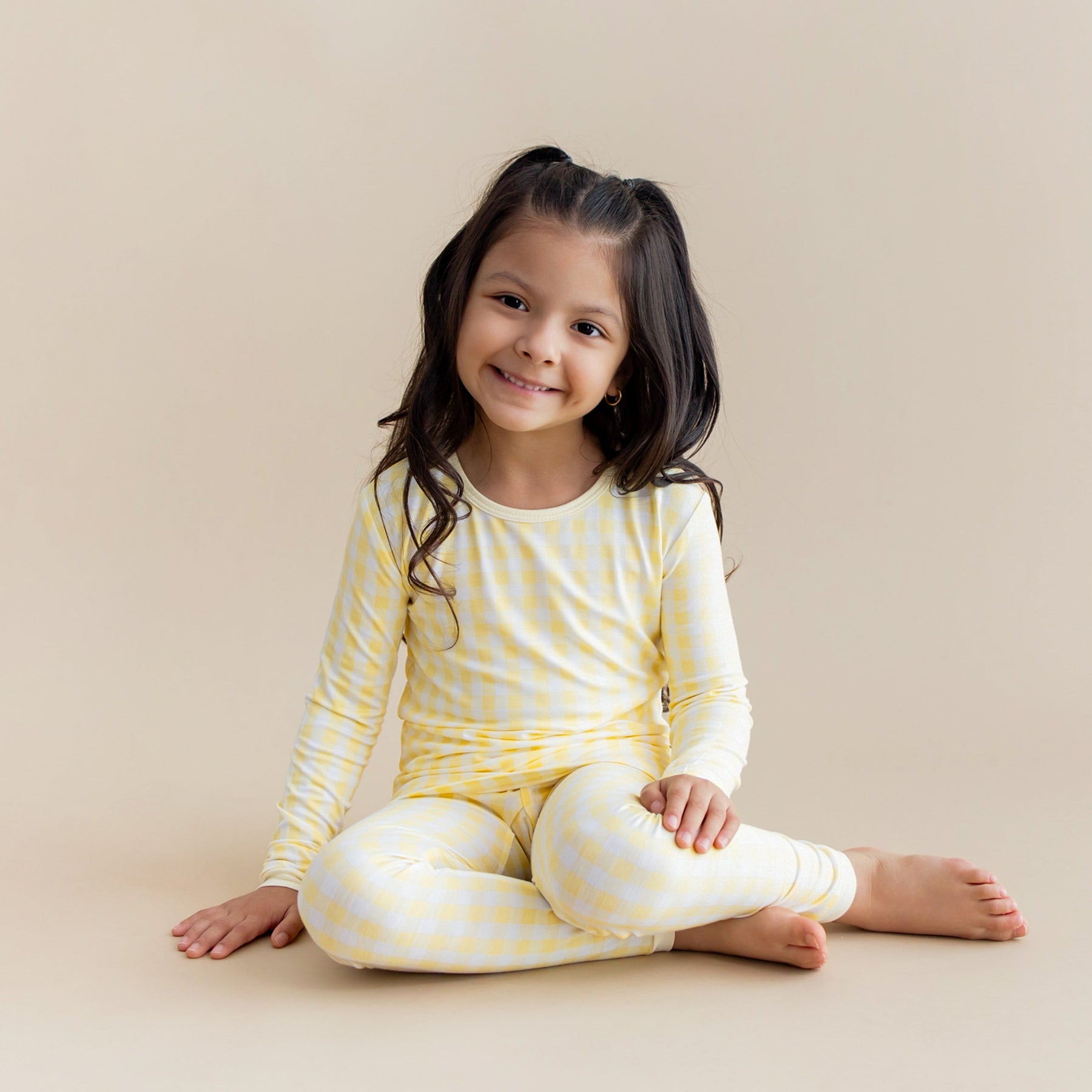 Young girl sitting on the floor wearing the Long Sleeve Pajamas in Gingham Chamomile