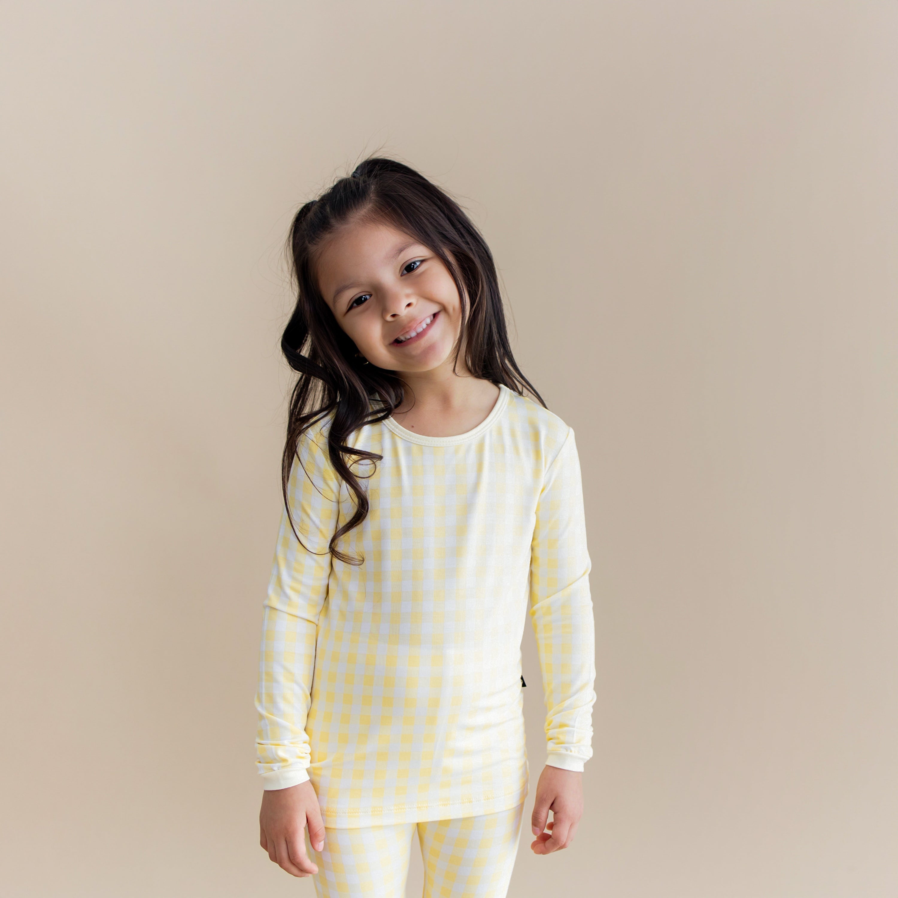 Young girl wearing the Long Sleeve Pajamas in Gingham Chamomile standing in front of a light beige background