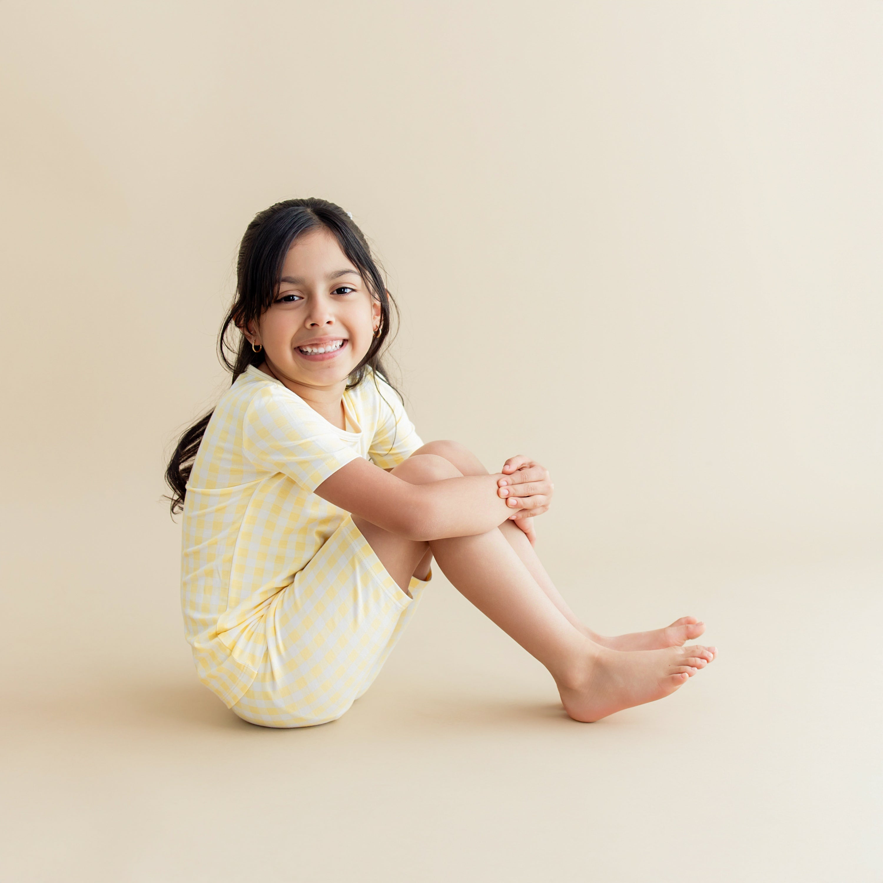 Young girl sitting on the floor wearing the Short Sleeve Pajamas in Gingham Chamomile