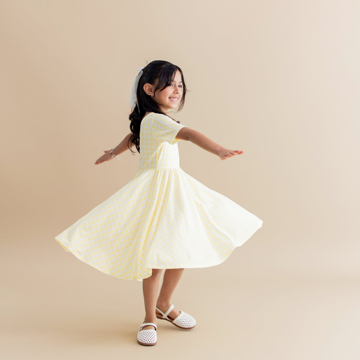 Young girl twirling in the Twirl Dress in Gingham Chamomile