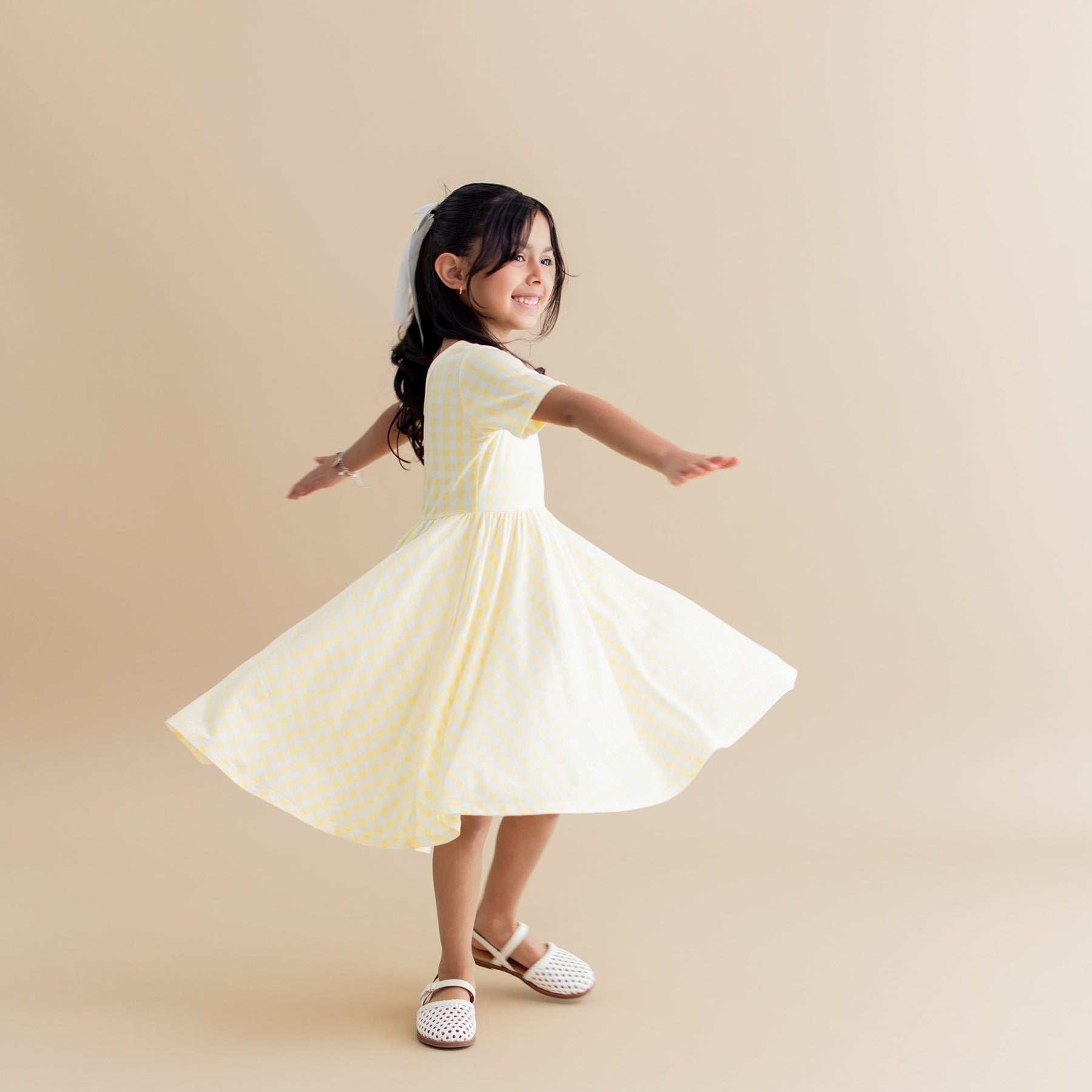 Young girl twirling in the Twirl Dress in Gingham Chamomile