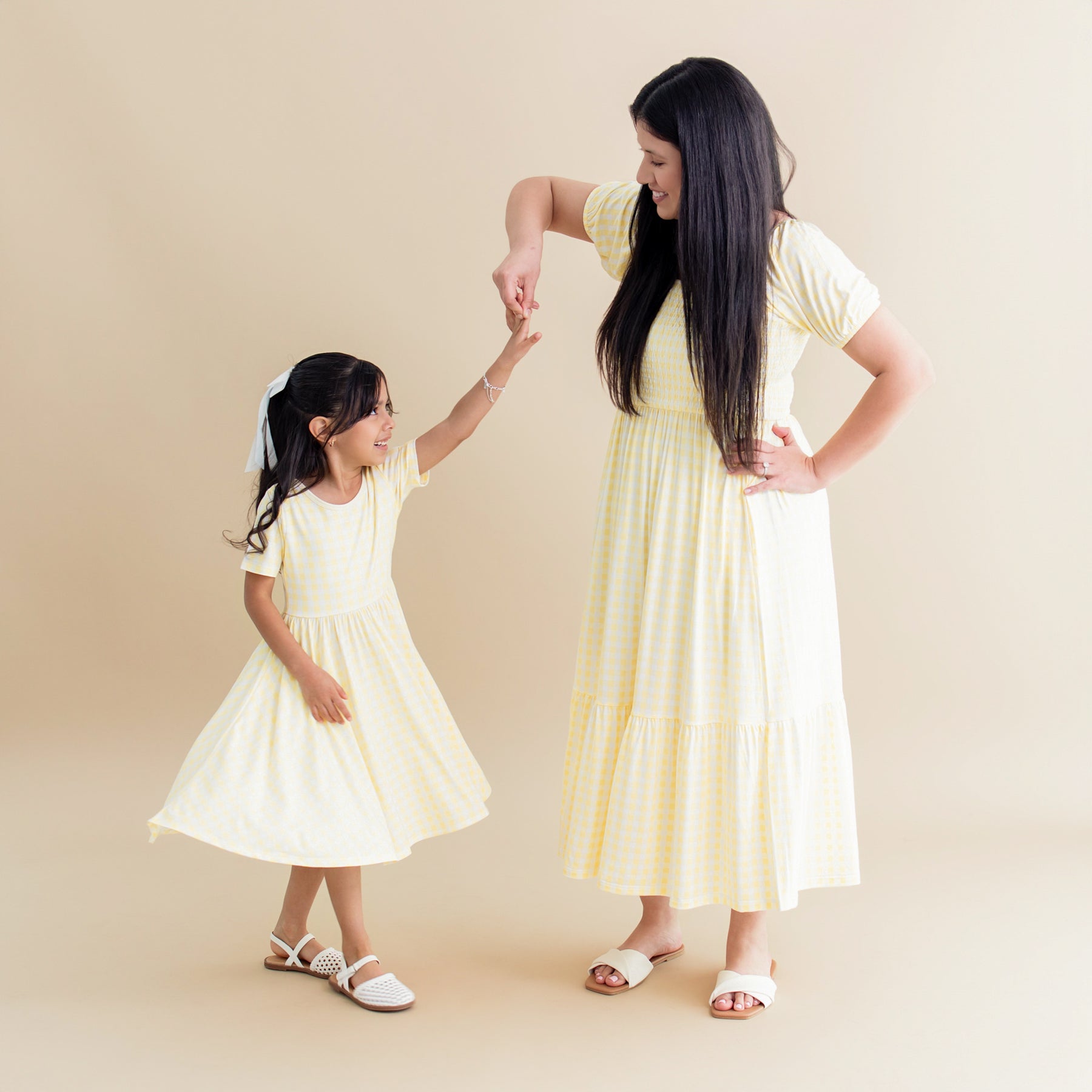 Young girl wearing the Twirl Dress in Gingham Chamomile being twirled by her mother wearing the matching women's smocked dress