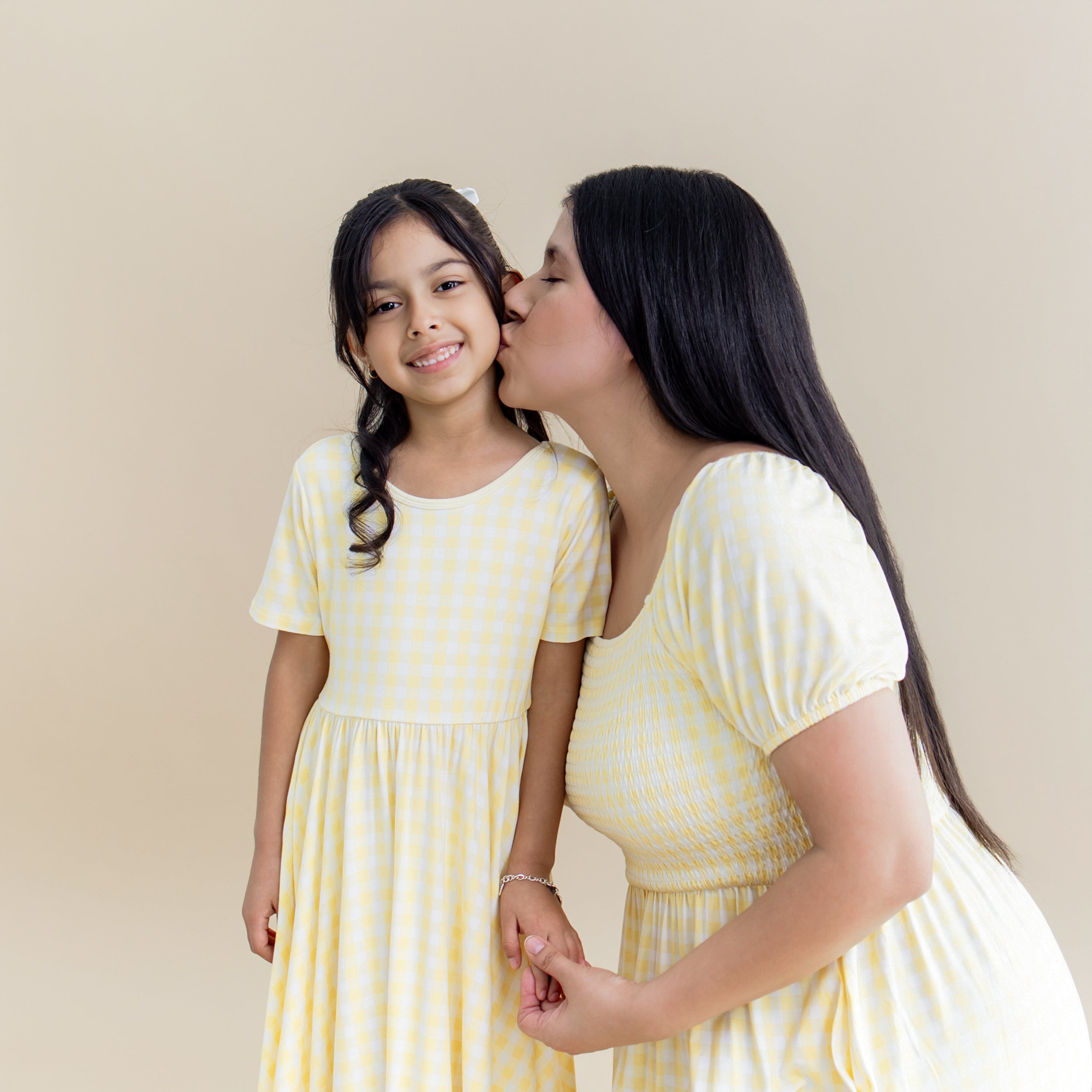 Young girl wearing the Twirl Dress in Gingham Chamomile standing beside her mother wearing the matching women's smocked dress