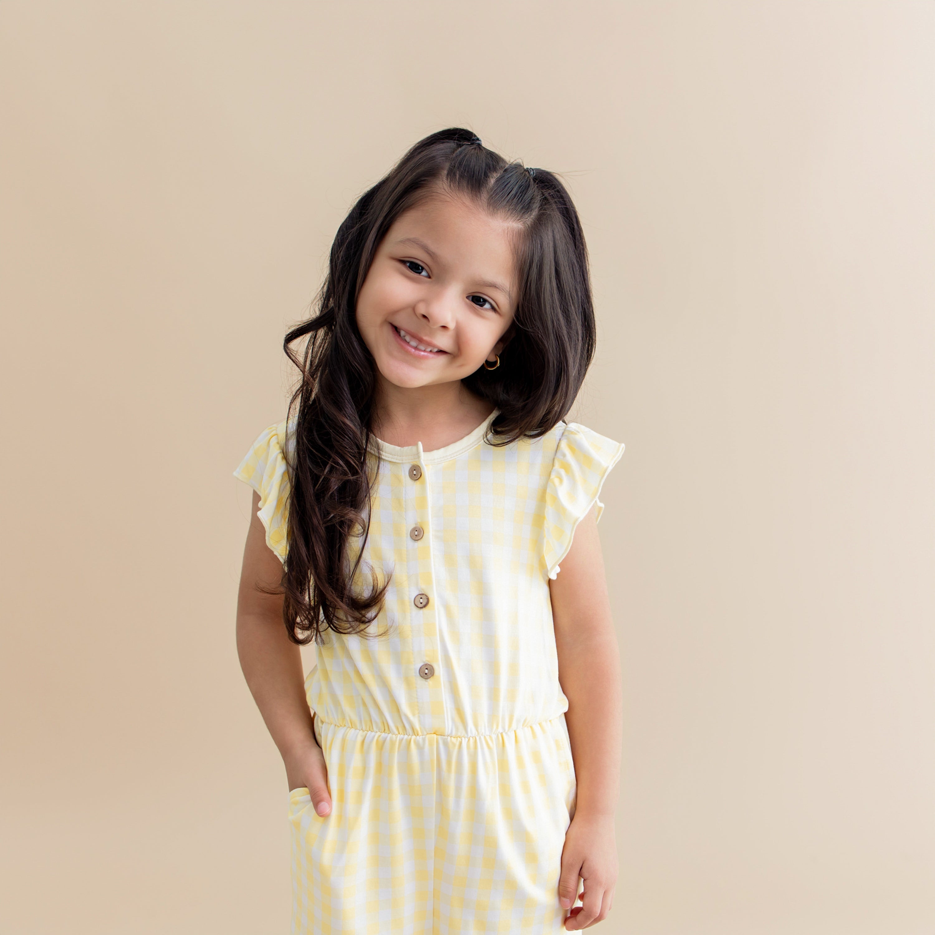 Close up of a young girl posing with her hand in the pocket of the Flutter Sleeve Romper in Gingham Chamomile