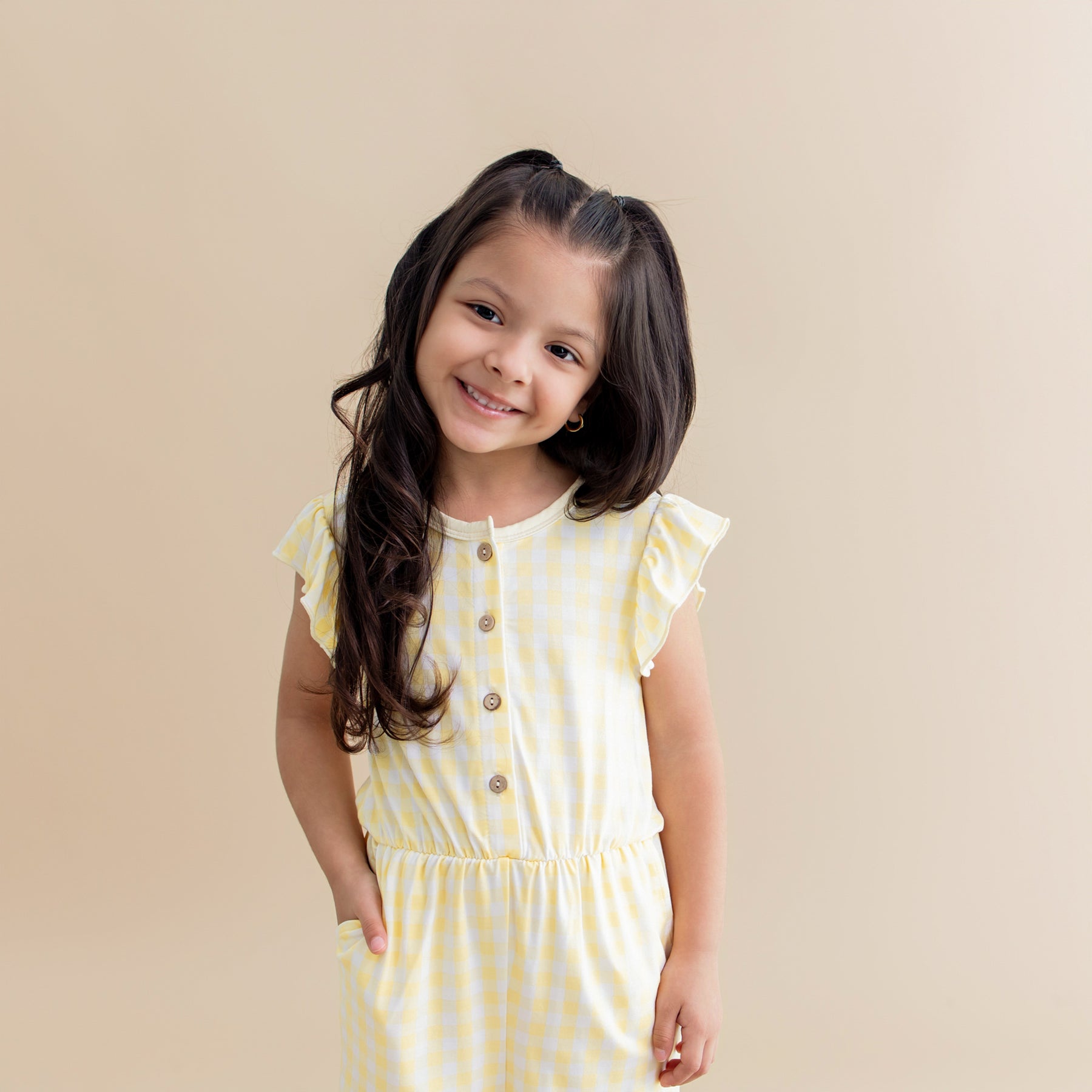Close up of a young girl posing with her hand in the pocket of the Flutter Sleeve Romper in Gingham Chamomile