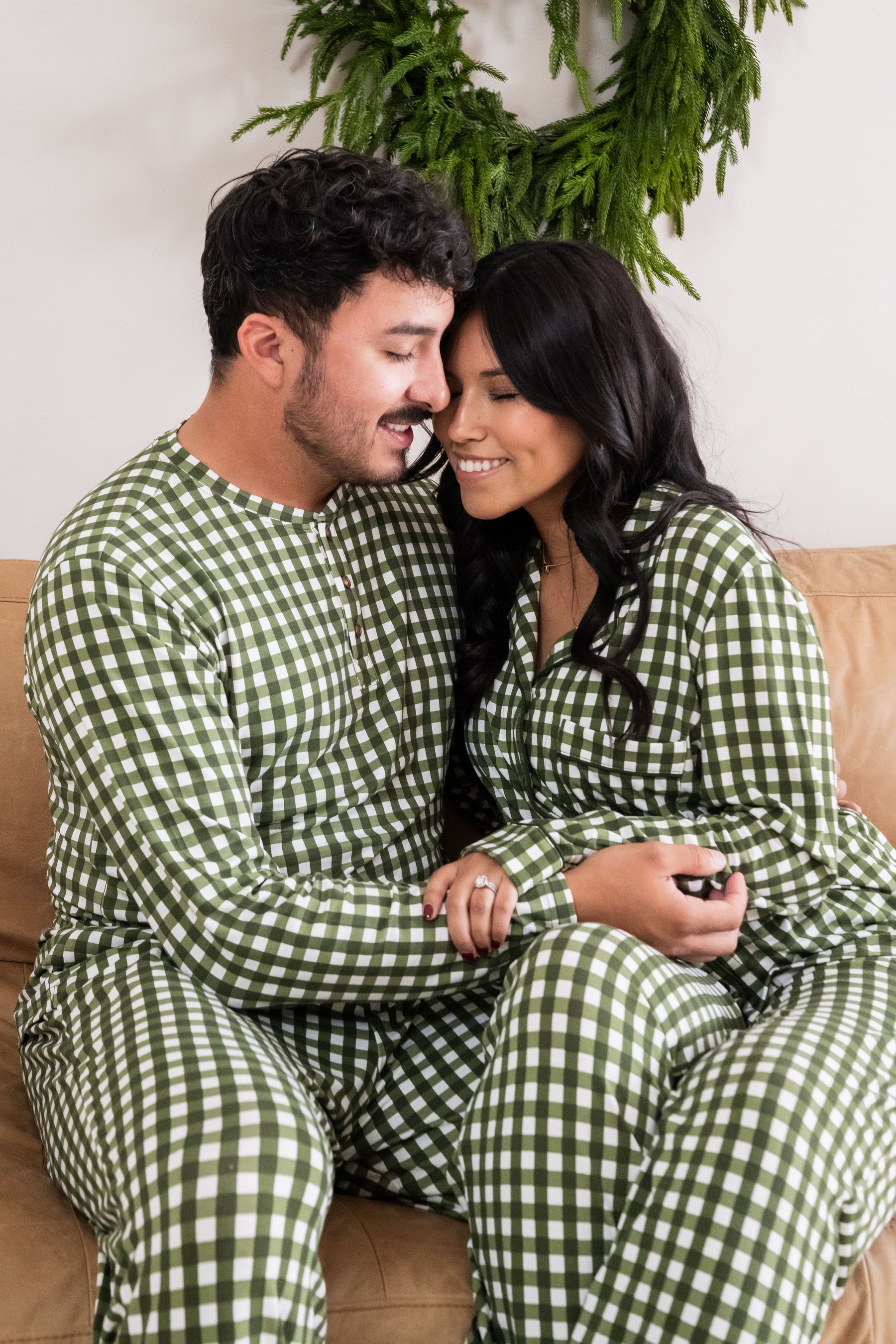 Husband and wife sitting on a brown leather couch matching in Gingham Fir pajamas