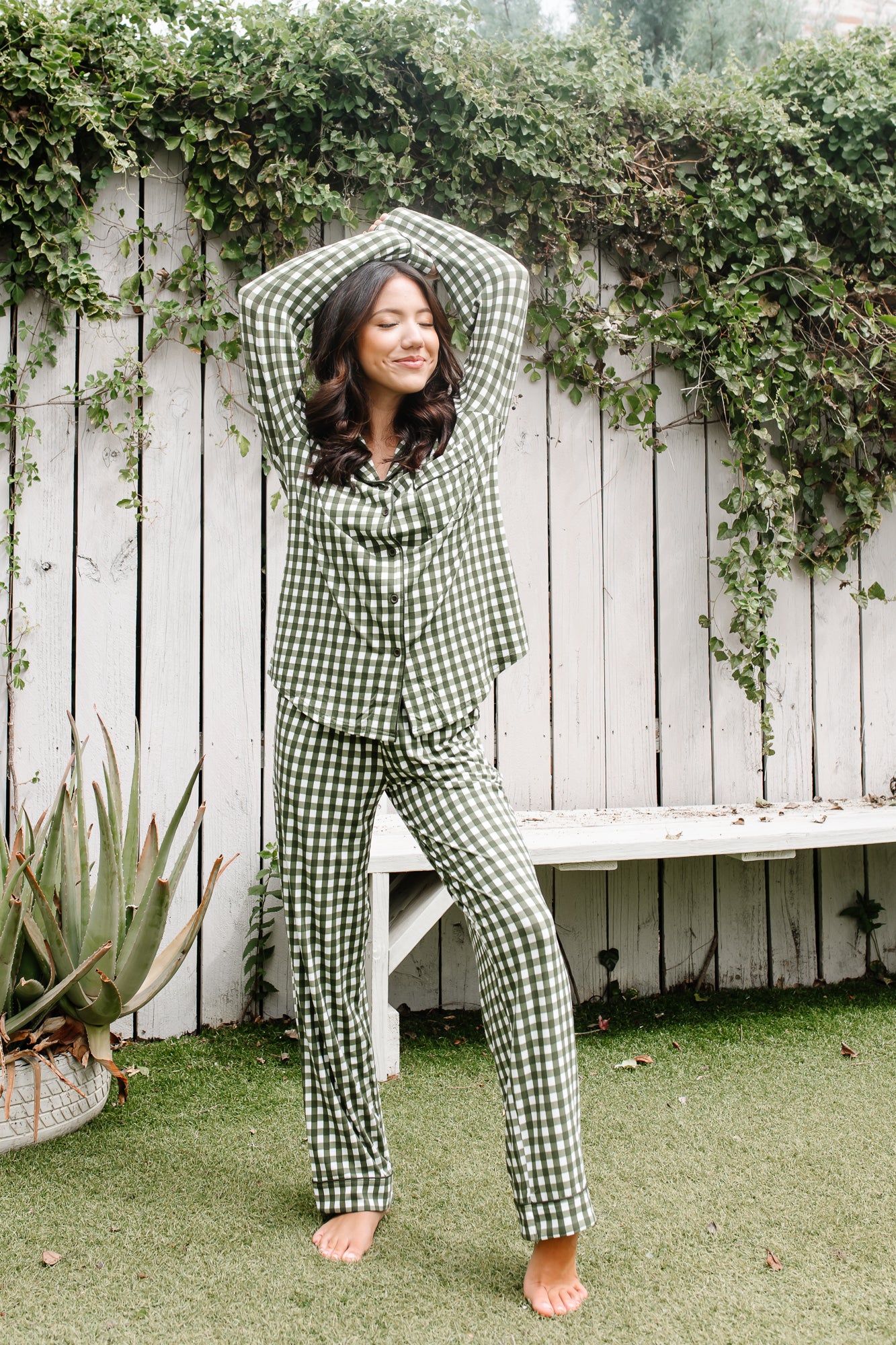 Smiling female wearing the Long-Sleeved Women's Pajama Set in Gingham Fir with her hands clasped together over her head wearing the Long-Sleeved Women's Pajama Set in Gingham Fir