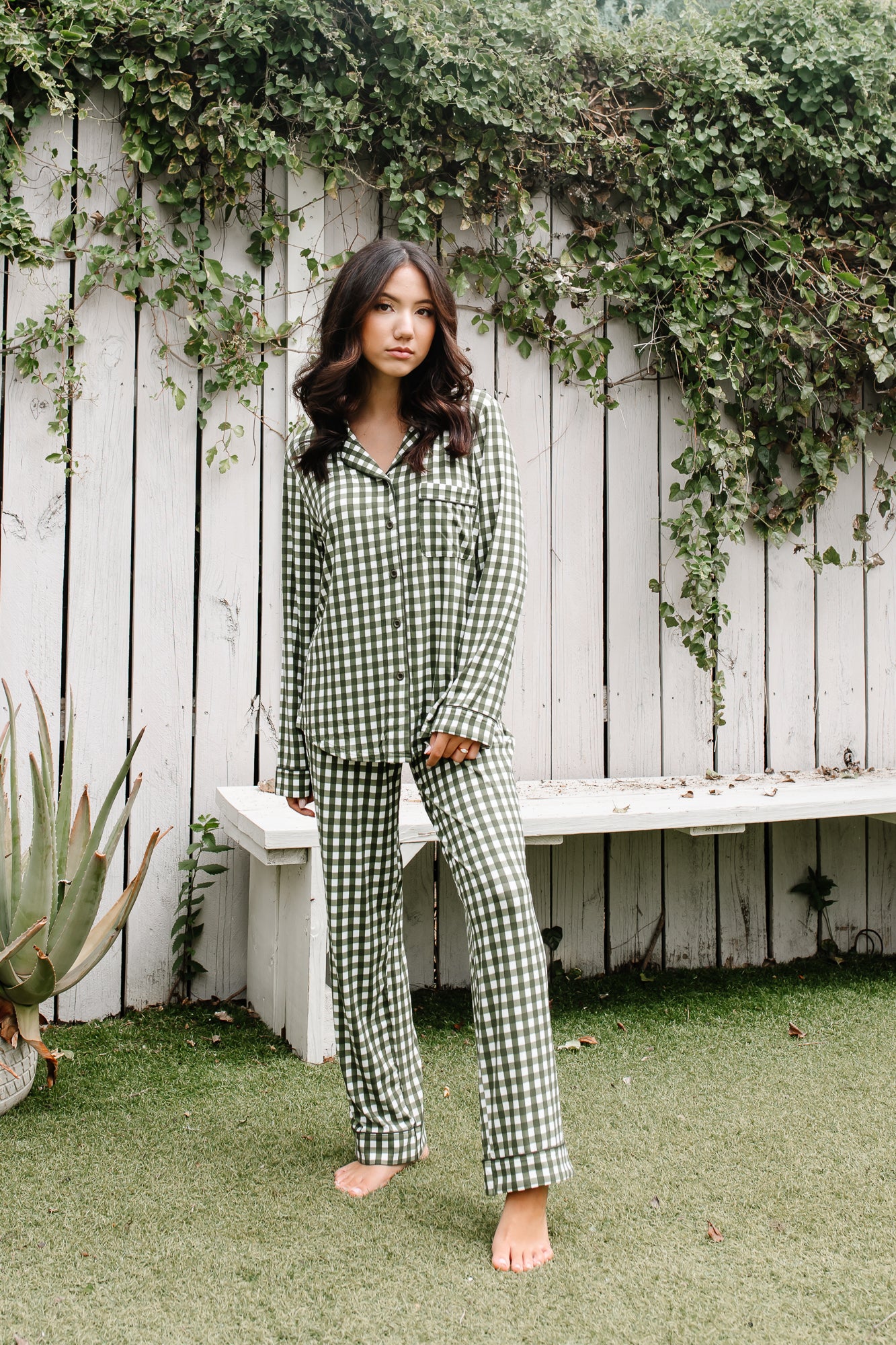 Female wearing the Long-Sleeved Women's Pajama Set in Gingham Fir standing in front of a white wooden fence