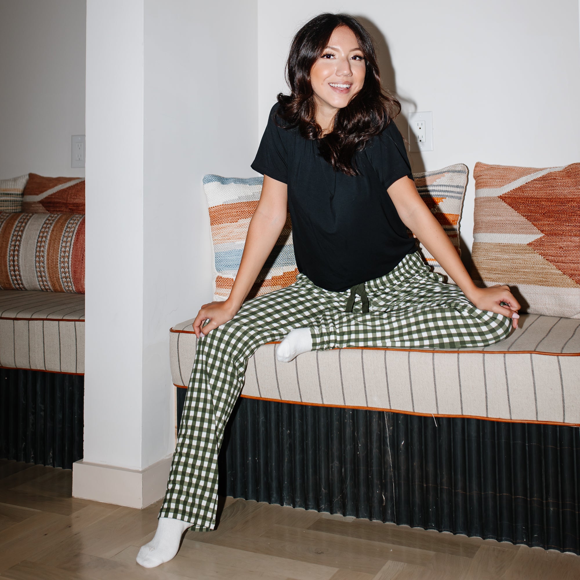 Female model sitting on a bench wearing the Women's Lounge Pants in Gingham Fir paired with a Midnight Women's Crew Neck Tee