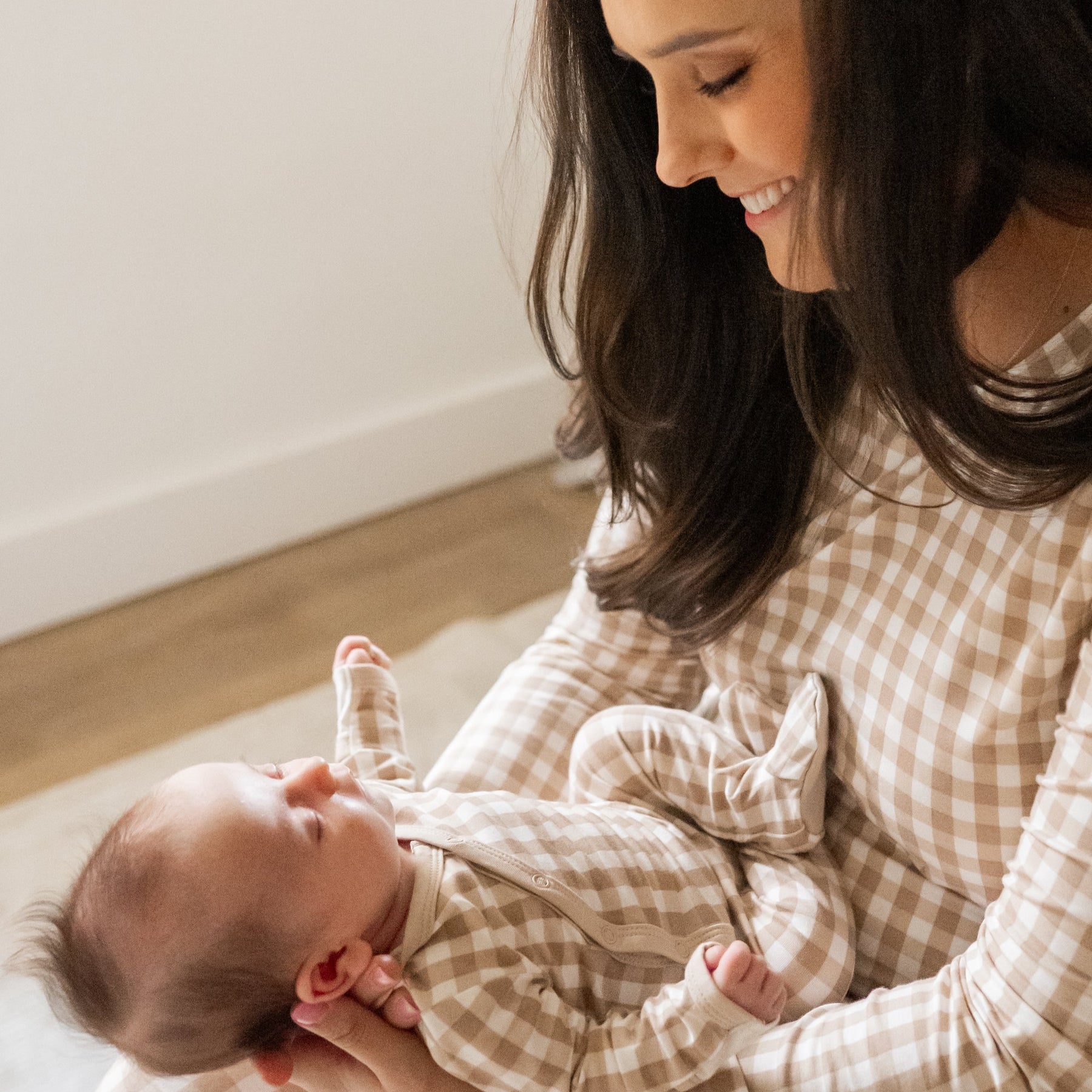 Mother wearing the Women's Jogger Pajama Set in Bisque Gingham holding newborn infant looking down and smiling at her