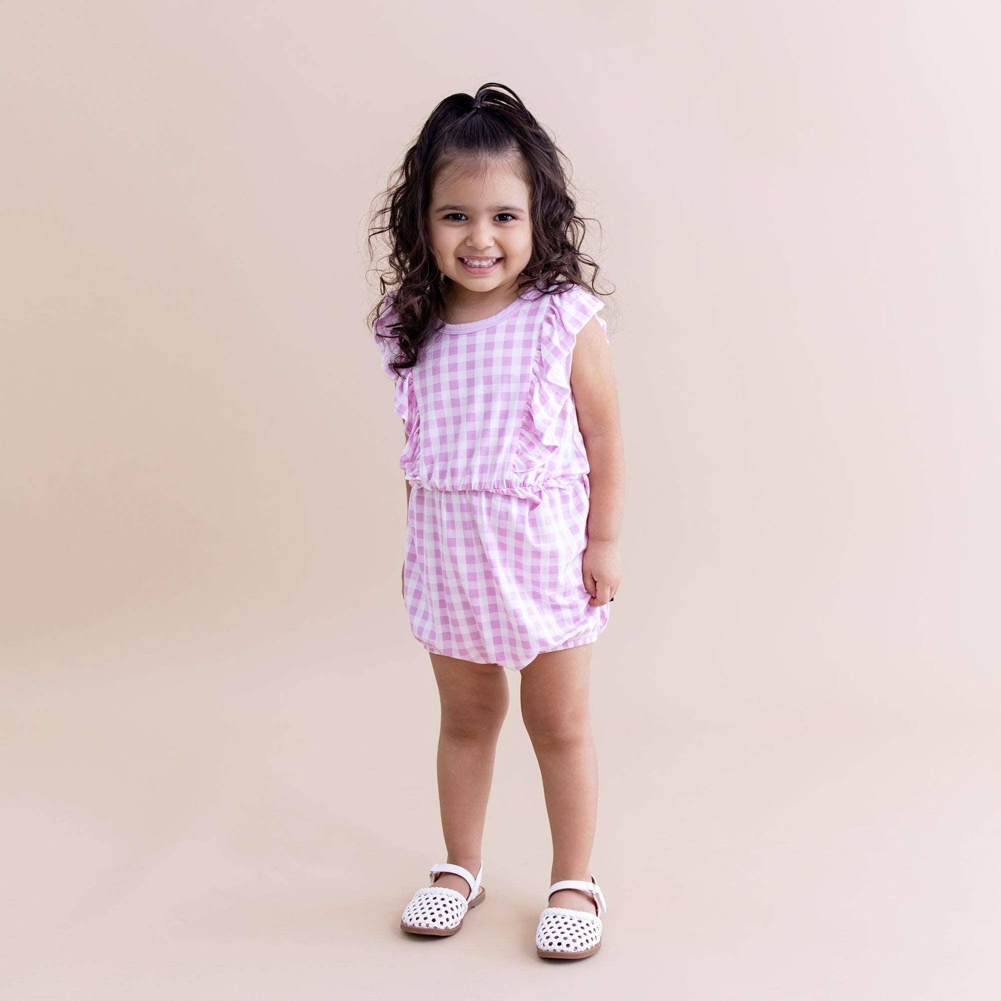 Young girl wearing the Bubble Romper in Gingham Thistle with white sandals