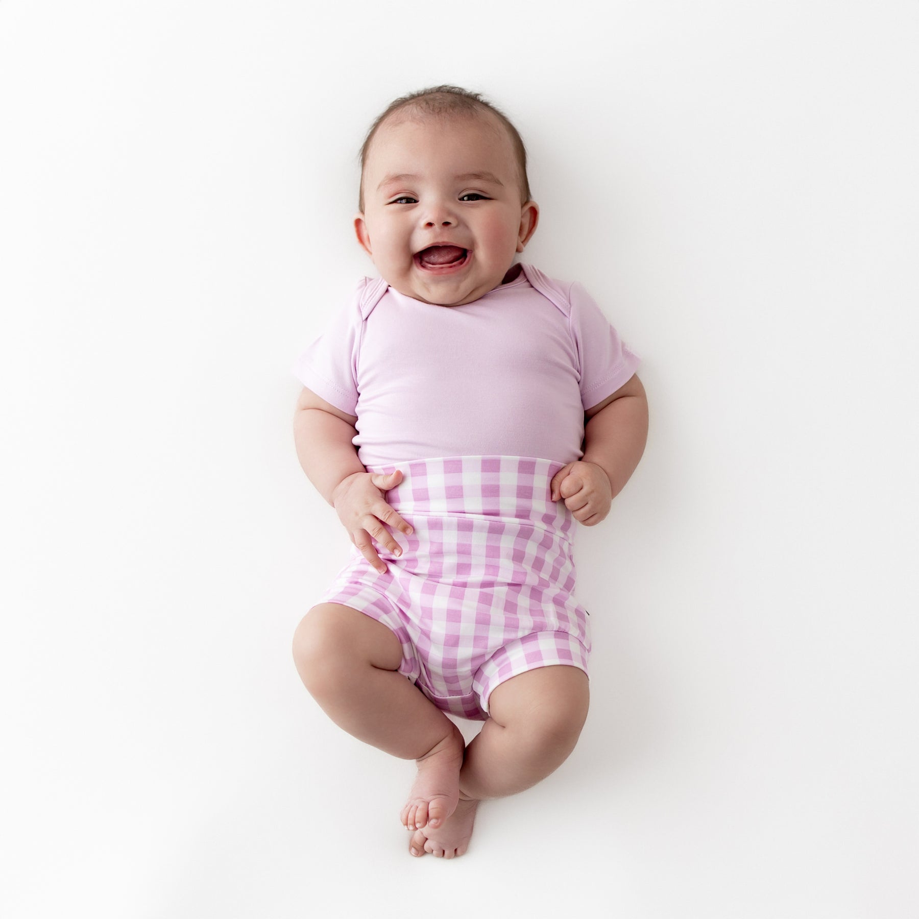 Smiling infant wearing the Bummies in Gingham Thistle paired with light purple short sleeve bodysuit